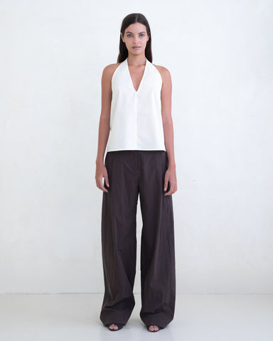 Woman wearing a cream halter top and brown wide-leg pants on a white background. 