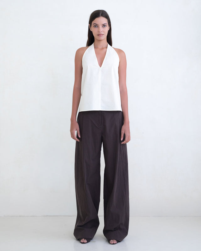 Woman wearing a cream halter top and brown wide-leg pants on a white background. 