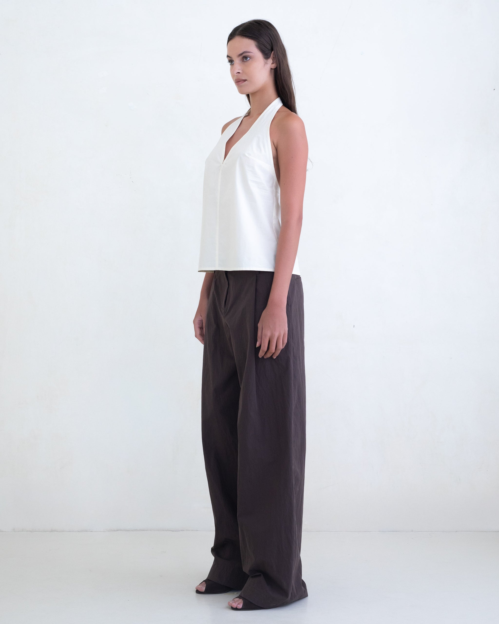 Woman wearing a cream halter top and brown wide-leg pants on a white background. 
