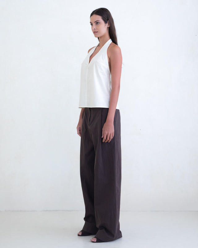 Woman wearing a cream halter top and brown wide-leg pants on a white background. 