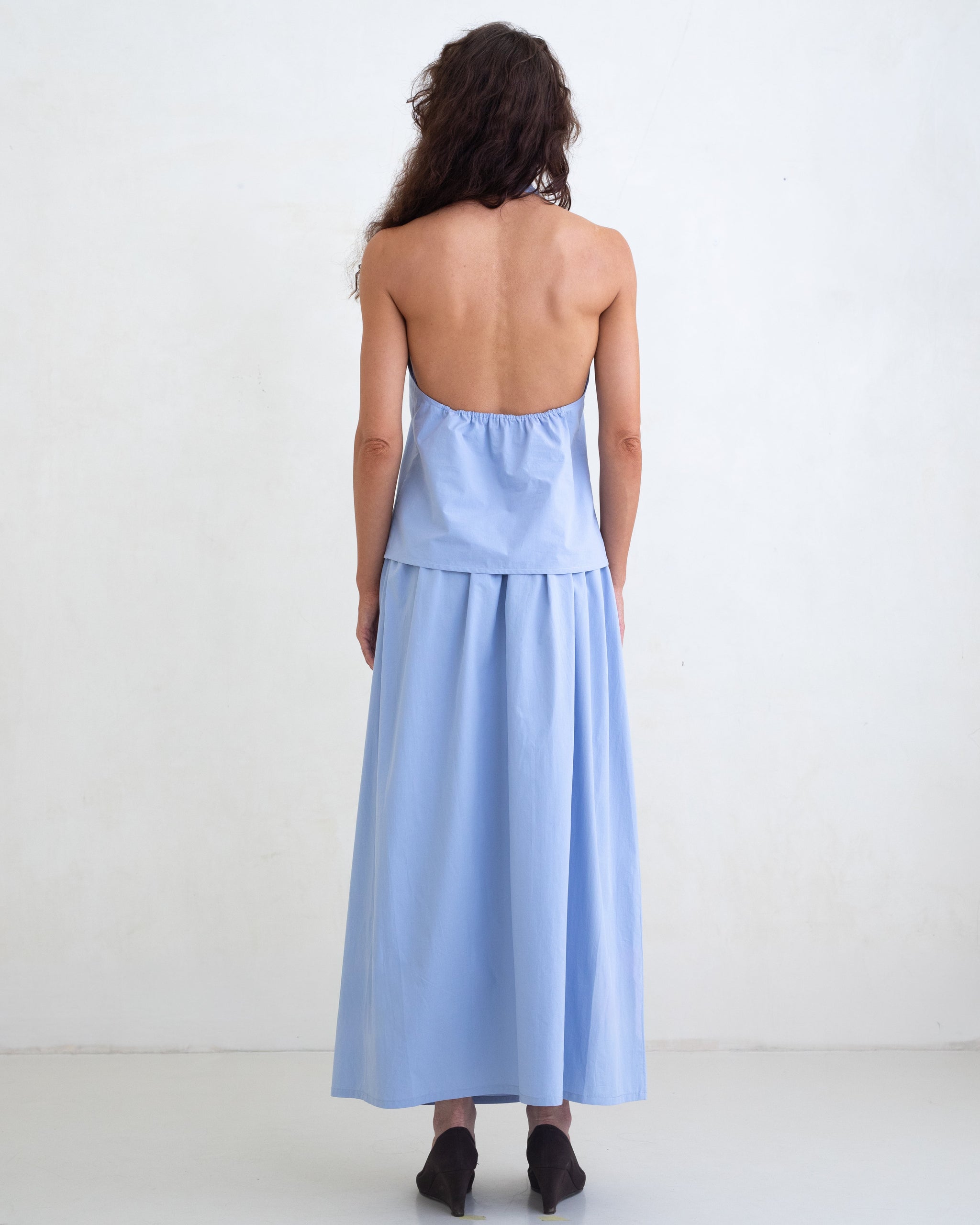 Woman wearing a light blue v-neck halter top and a matching light blue maxi skirt on a white background. 