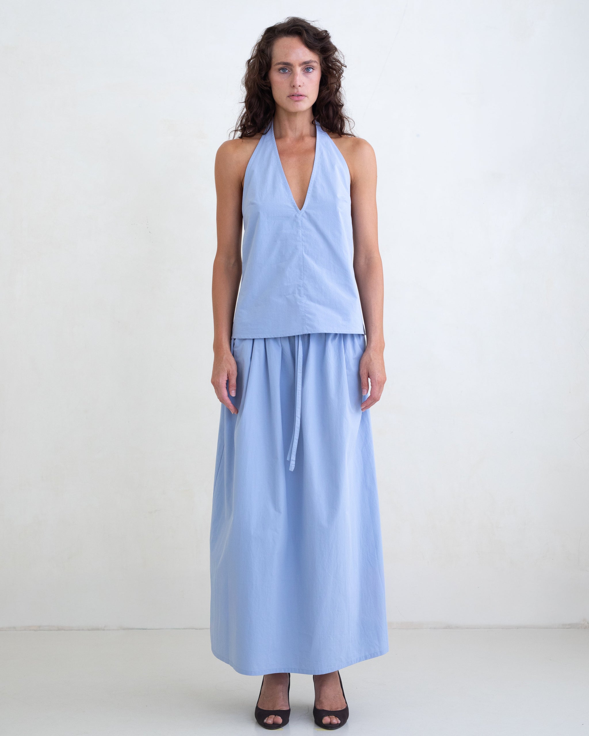 Woman wearing a light blue v-neck halter top and a matching light blue maxi skirt on a white background. 