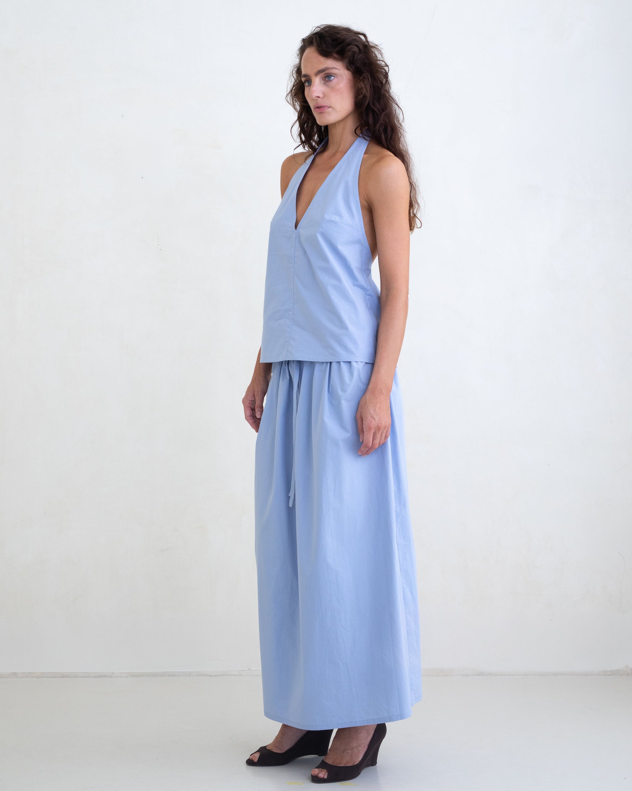 Woman wearing a light blue v-neck halter top and a matching light blue maxi skirt on a white background. 