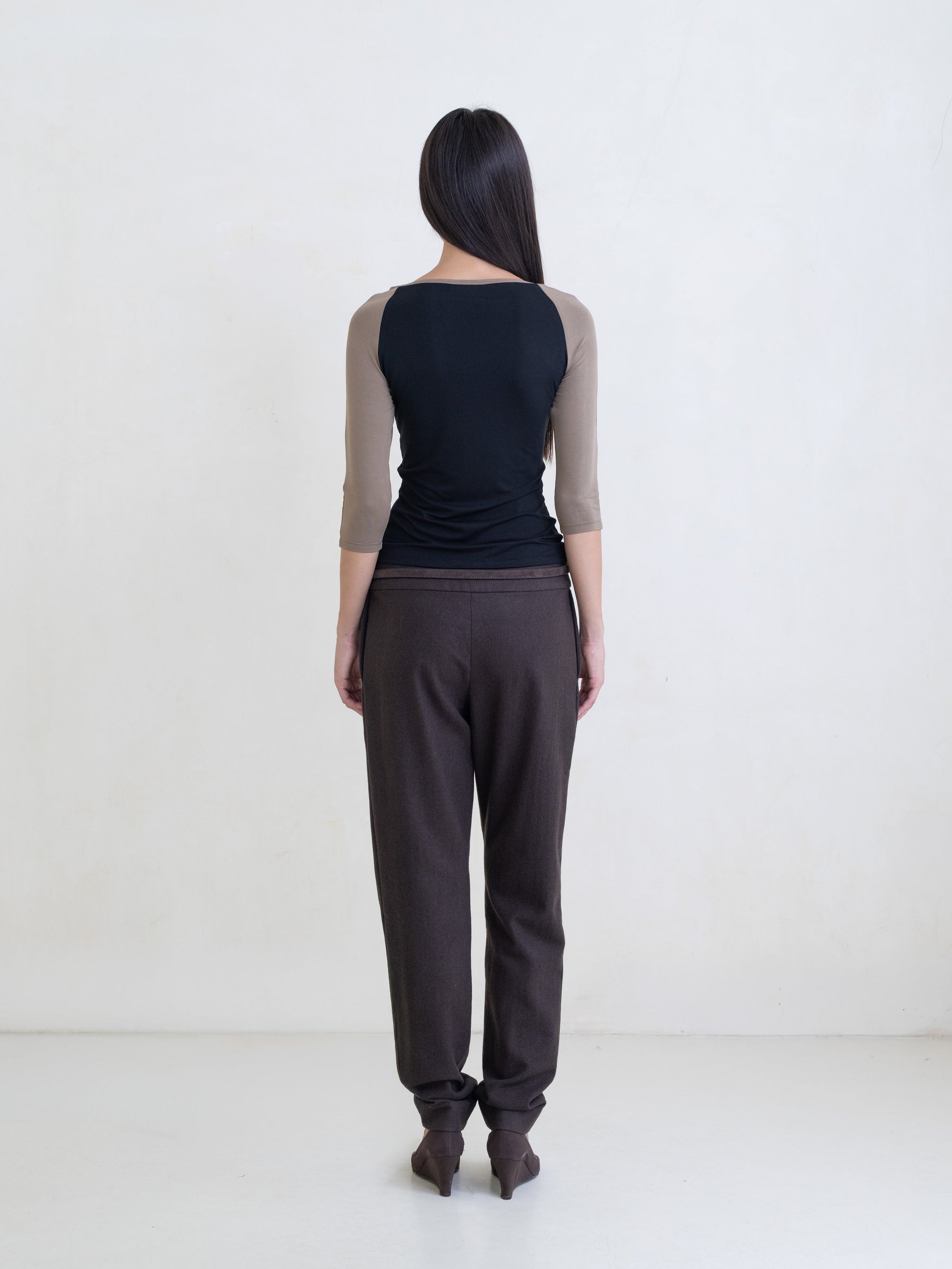 Woman wearing a black raglan top and brown pants on a white background. 