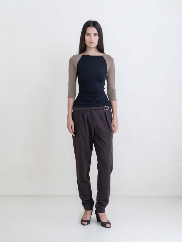 Woman wearing a black raglan top and brown pants on a white background. 