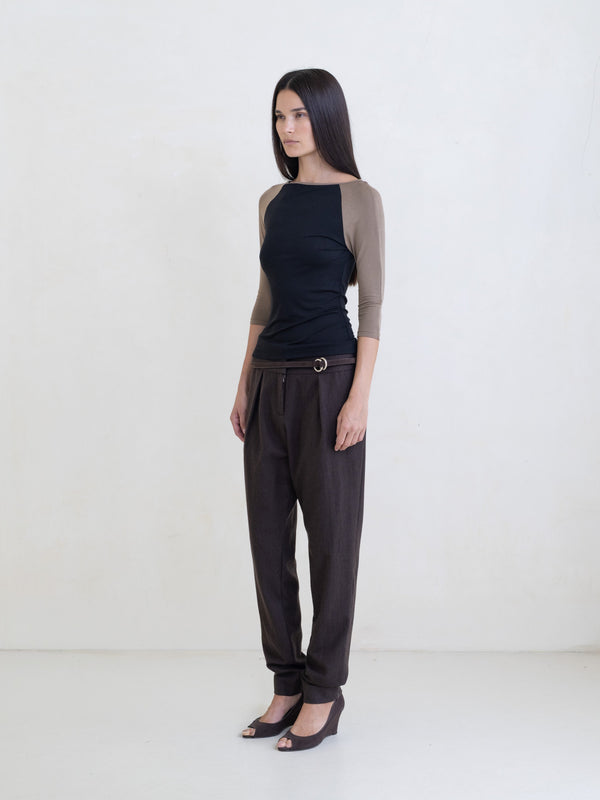 Woman wearing a black raglan top and brown pants on a white background. 