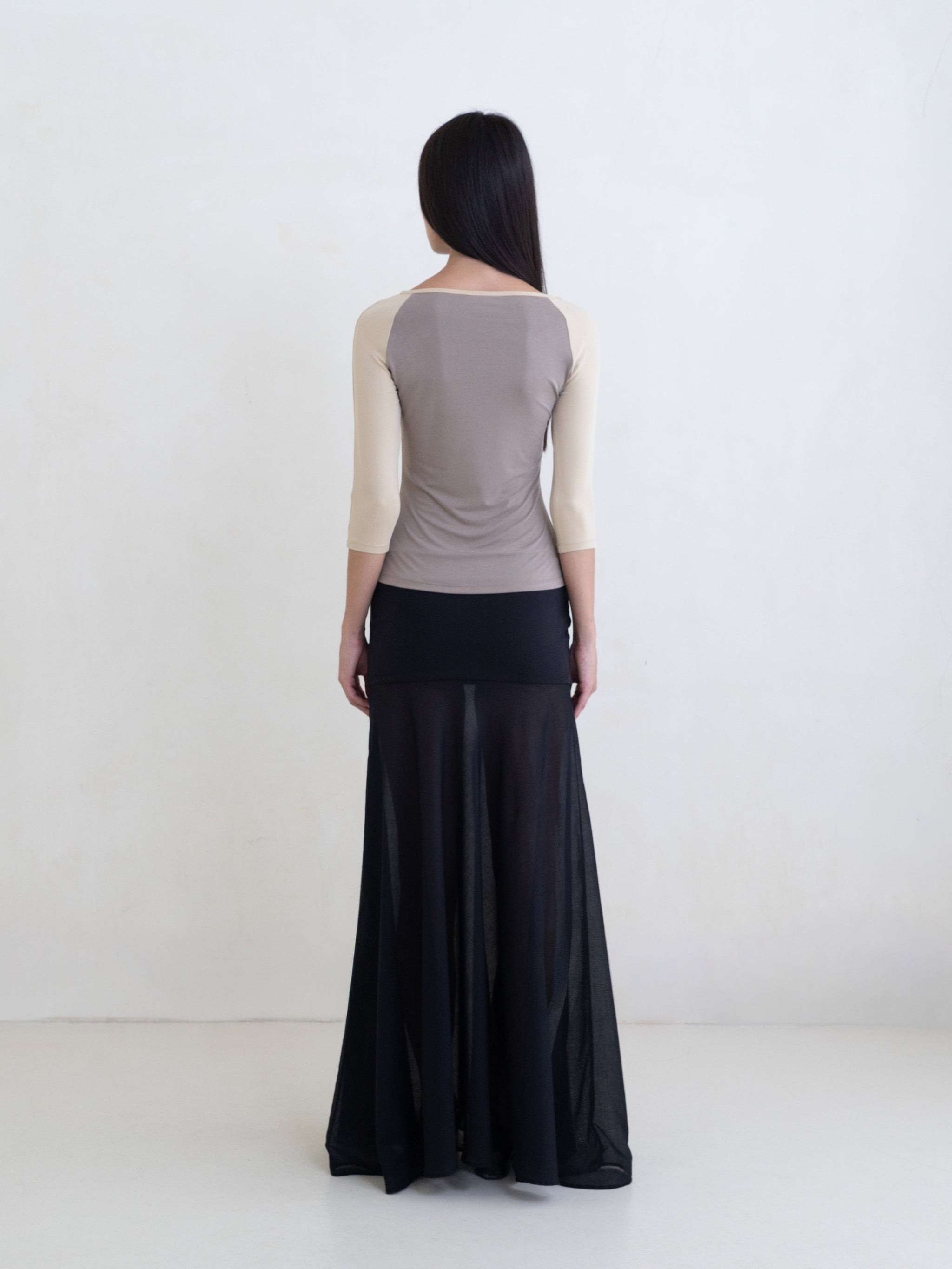 Woman wearing a taupe raglan top and a black maxi skirt on a white background. 