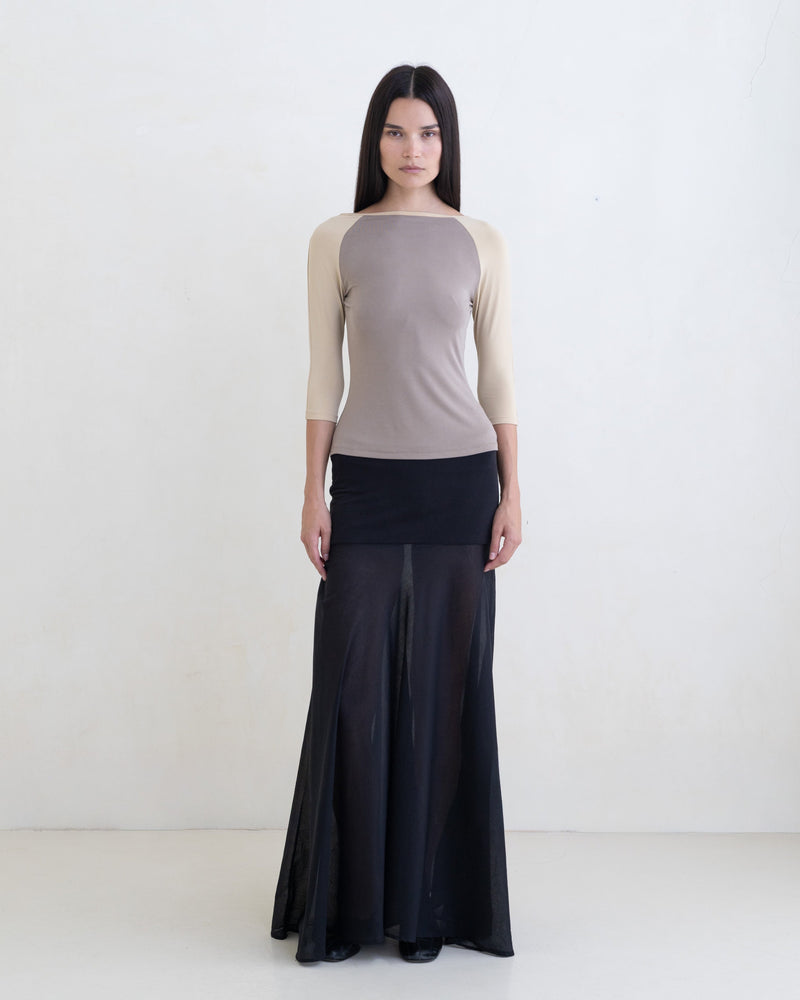 Woman wearing a taupe raglan top and a black maxi skirt on a white background. 