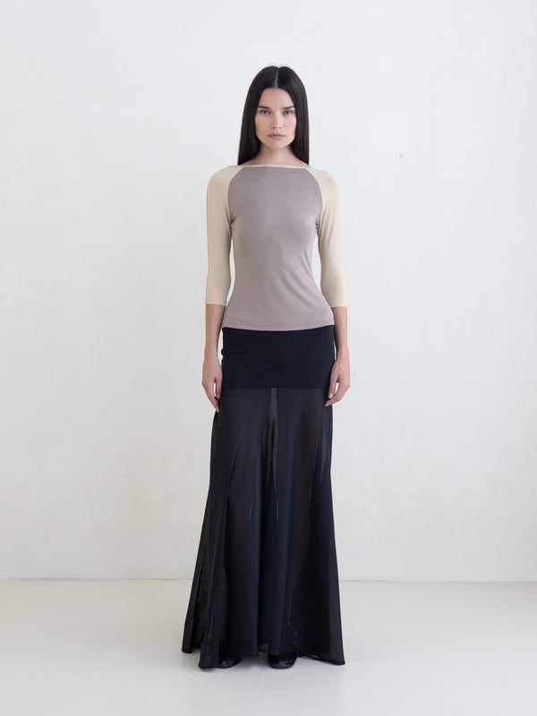 Woman wearing a taupe raglan top and a black maxi skirt on a white background. 