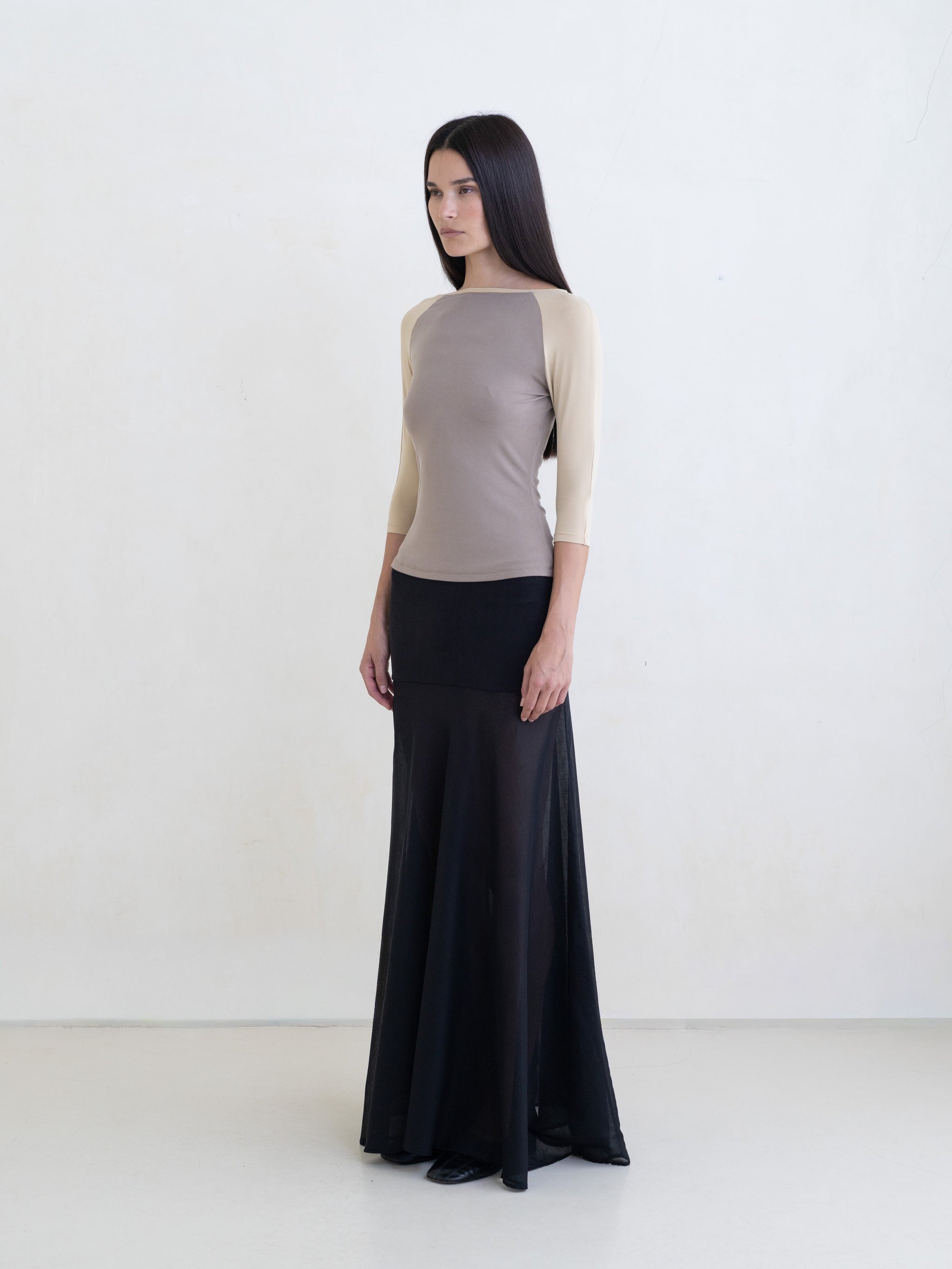 Woman wearing a taupe raglan top and a black maxi skirt on a white background. 