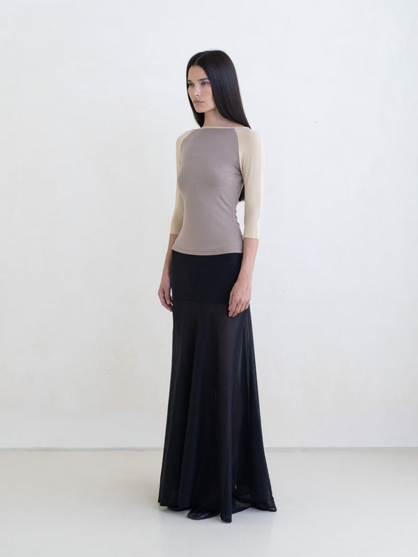 Woman wearing a taupe raglan top and a black maxi skirt on a white background. 