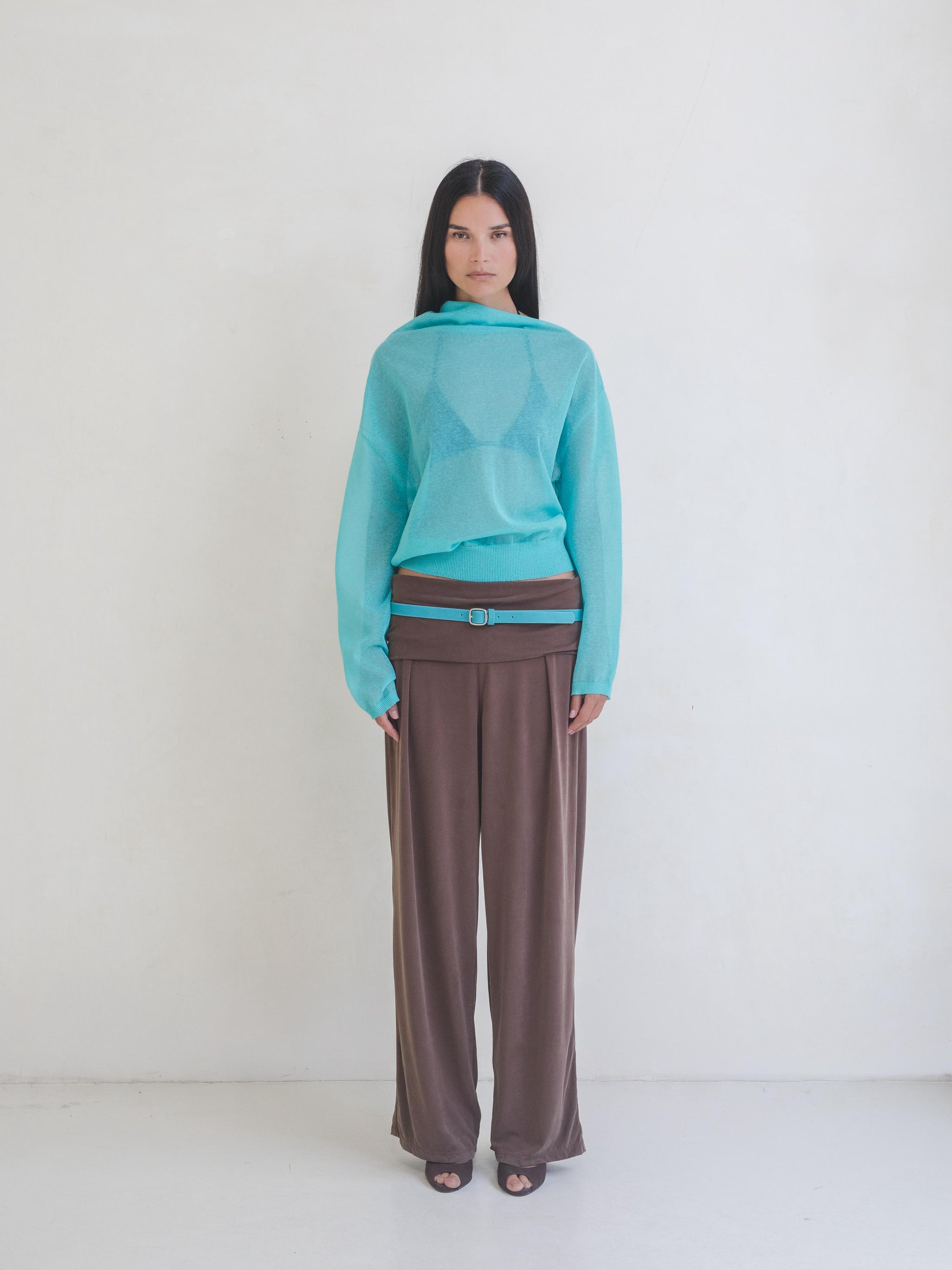 Woman wearing an aqua blue sheer sweater and brown pants on a white background.