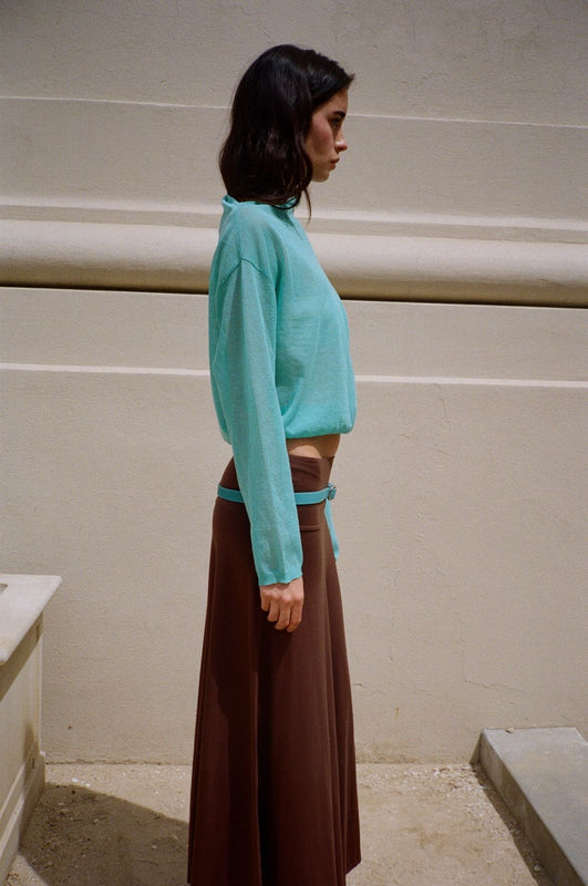 Woman wearing an aqua blue sheer sweater and brown pants on a beige background.