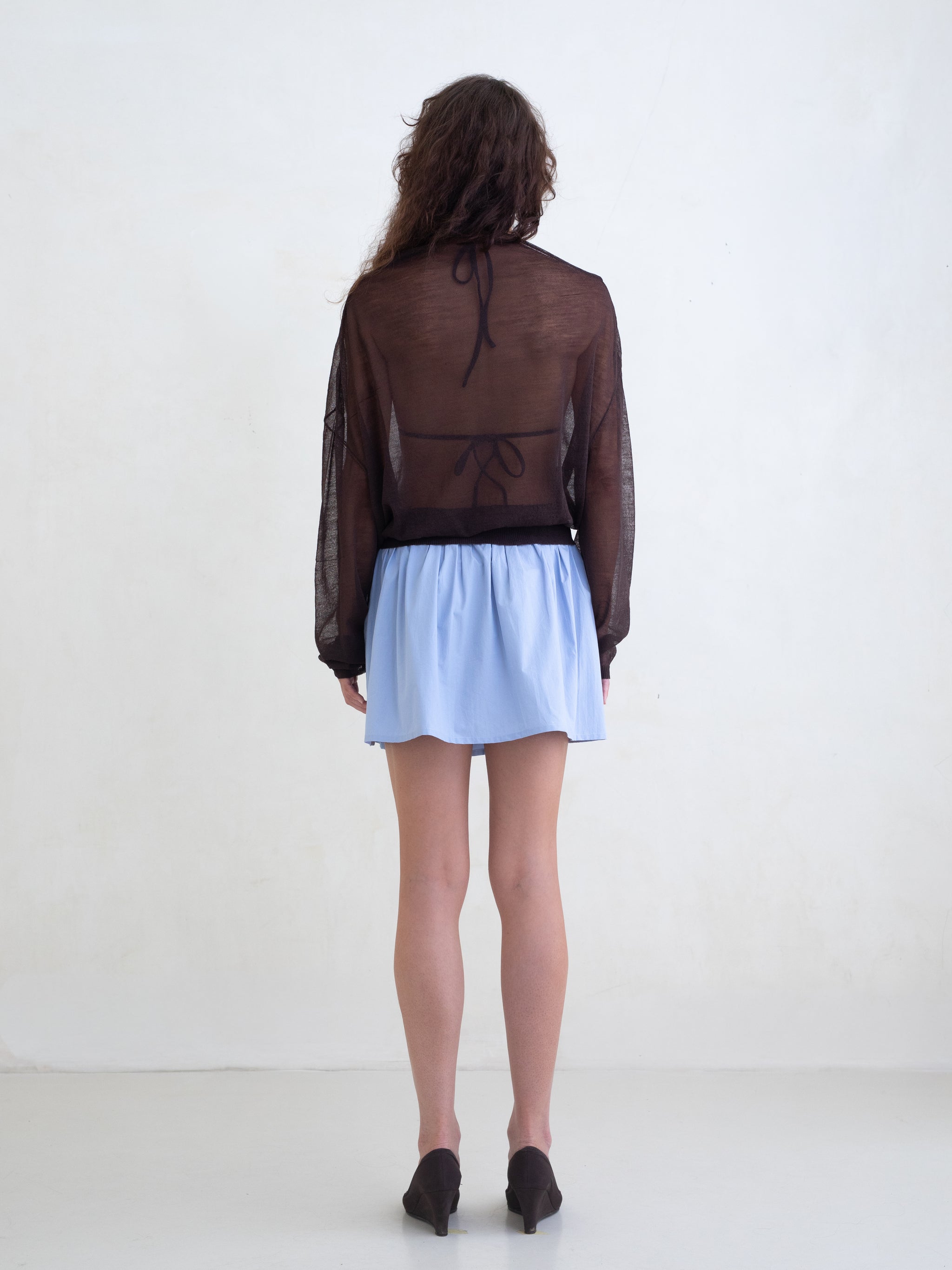 Woman wearing a brown sweater and a light blue mini skirt on a white background