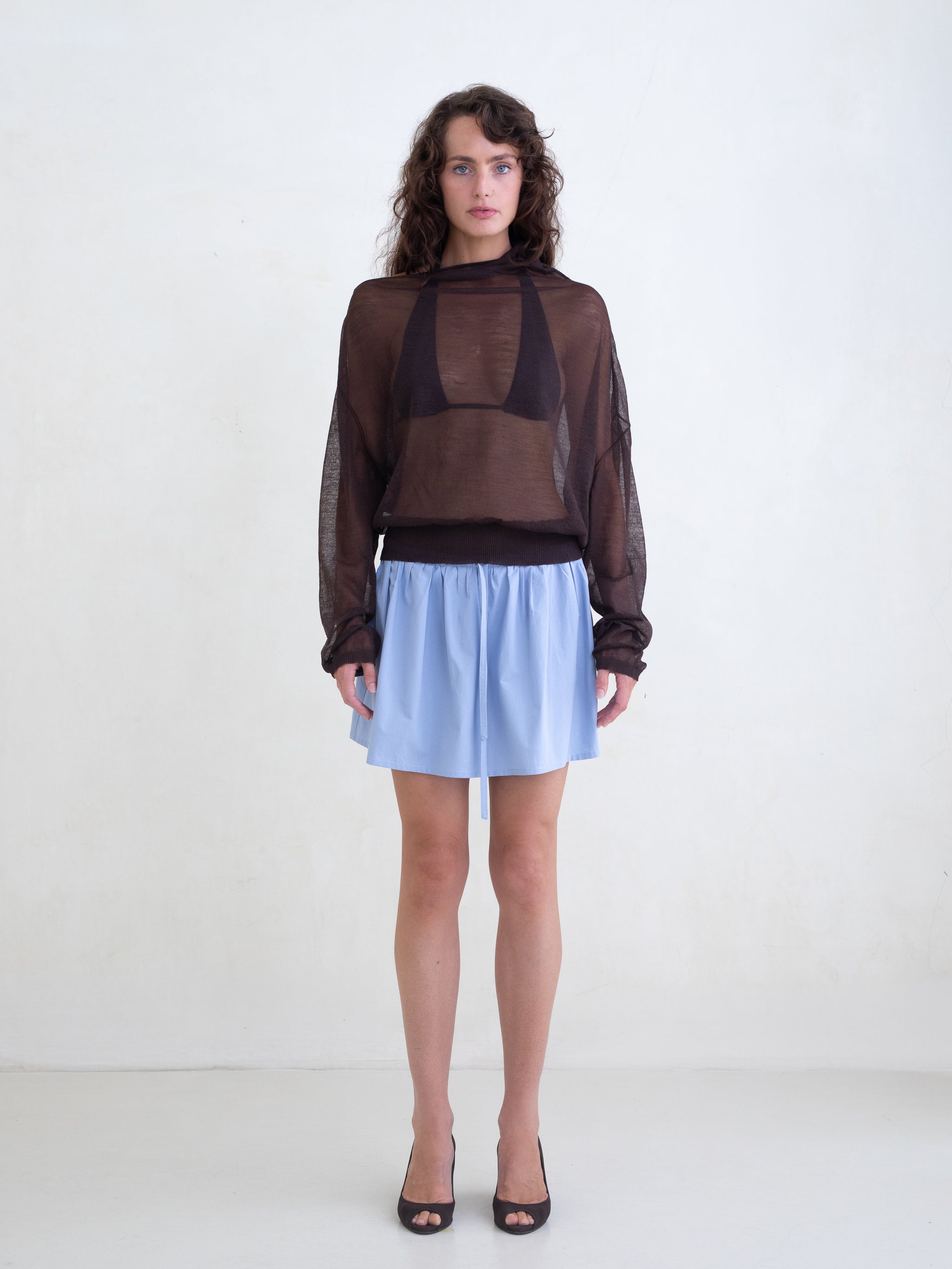 Woman wearing a brown sweater and a light blue mini skirt on a white background 