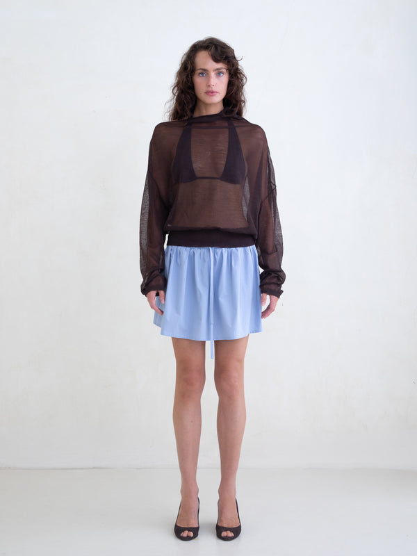 Woman wearing a brown sweater and a light blue mini skirt on a white background 