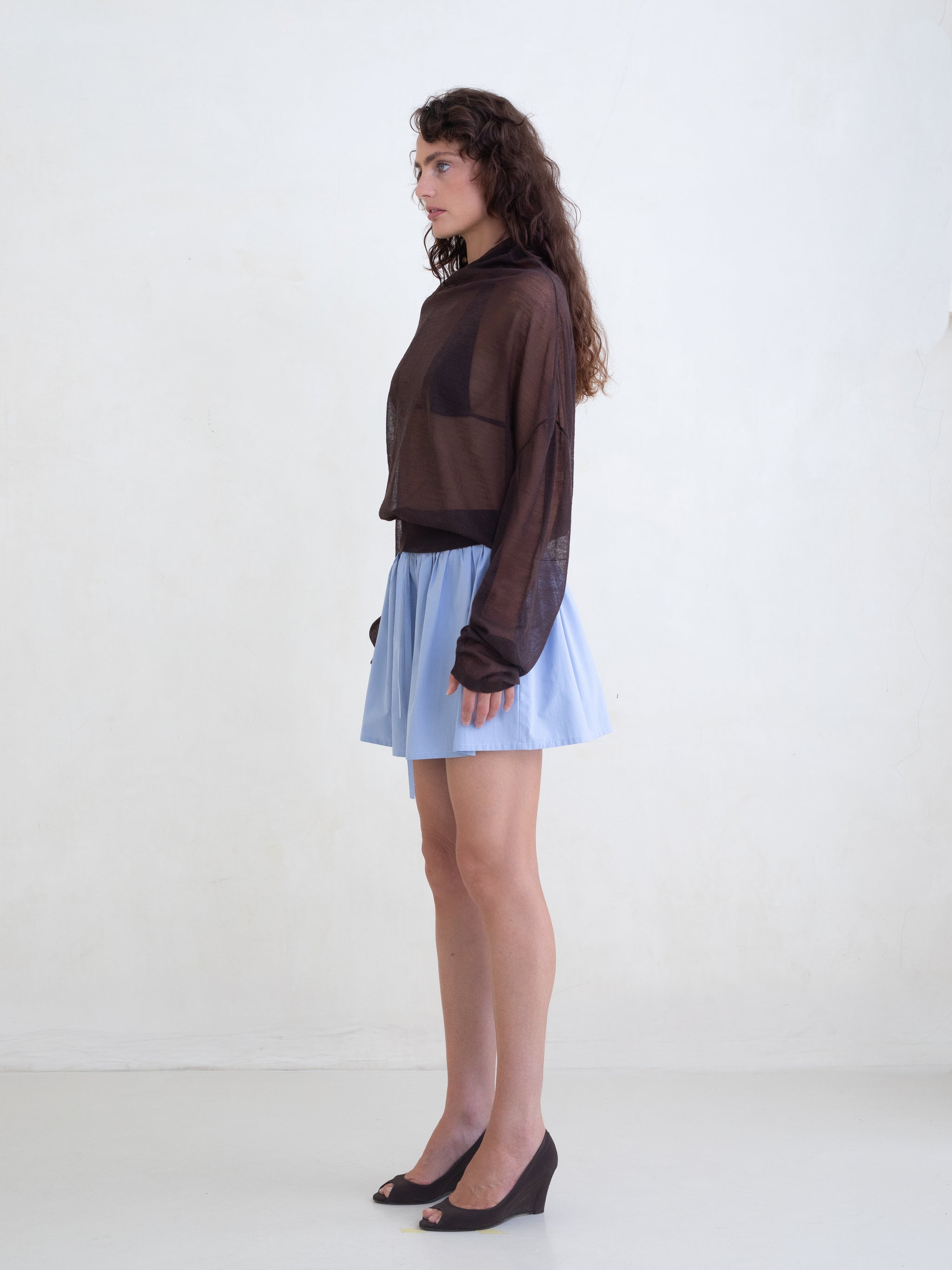 Woman wearing a brown sweater and a light blue mini skirt on a white background