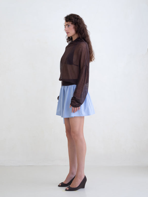 Woman wearing a brown sweater and a light blue mini skirt on a white background