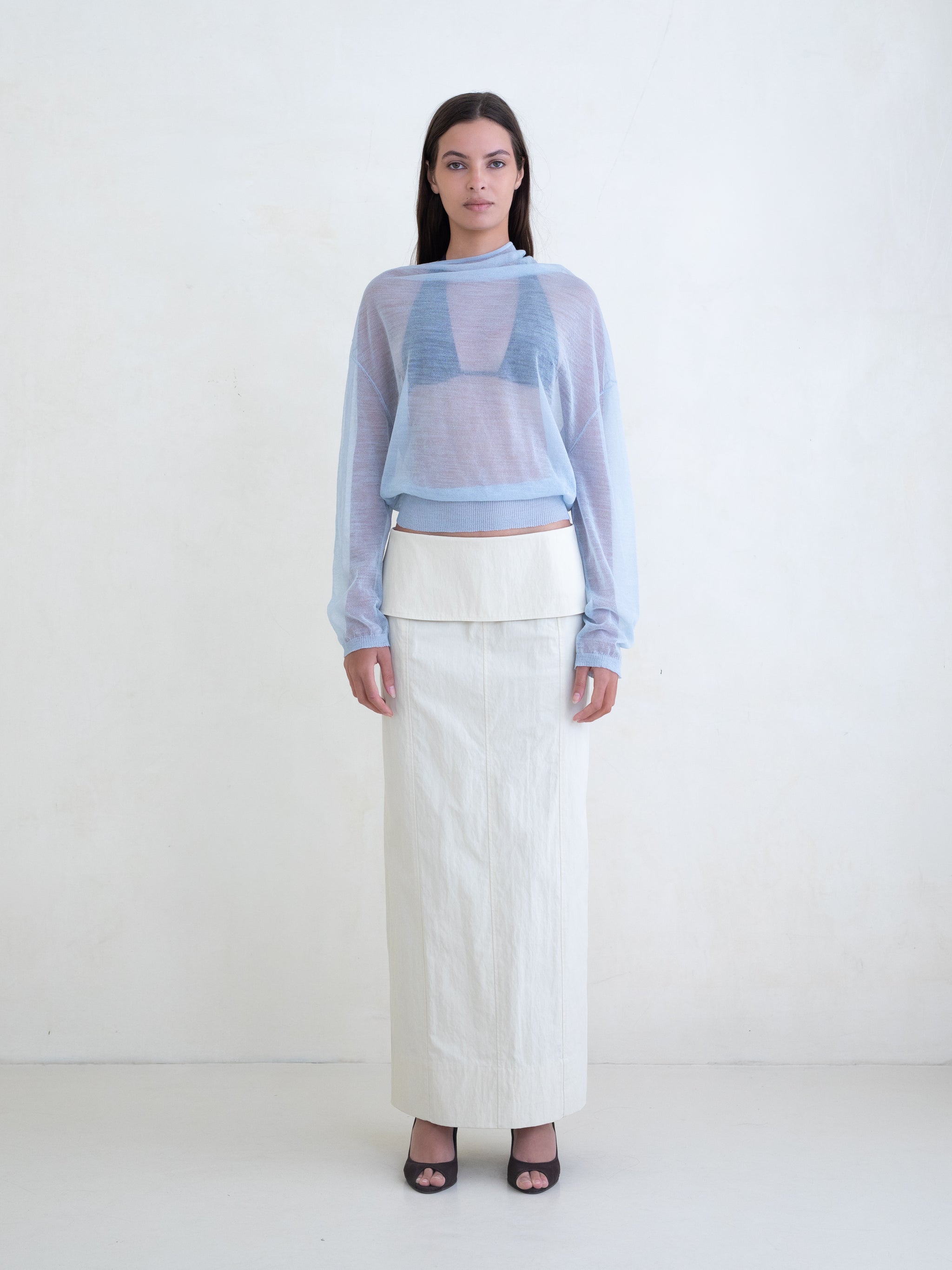 Woman wearing a light blue sweater and a cream skirt on a white background 