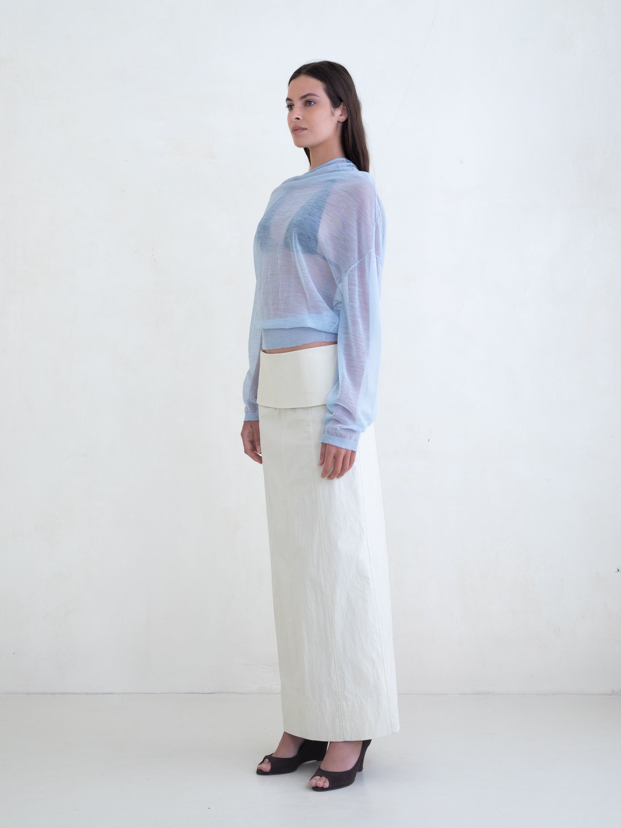 Woman wearing a light blue sweater and a cream skirt on a white background 