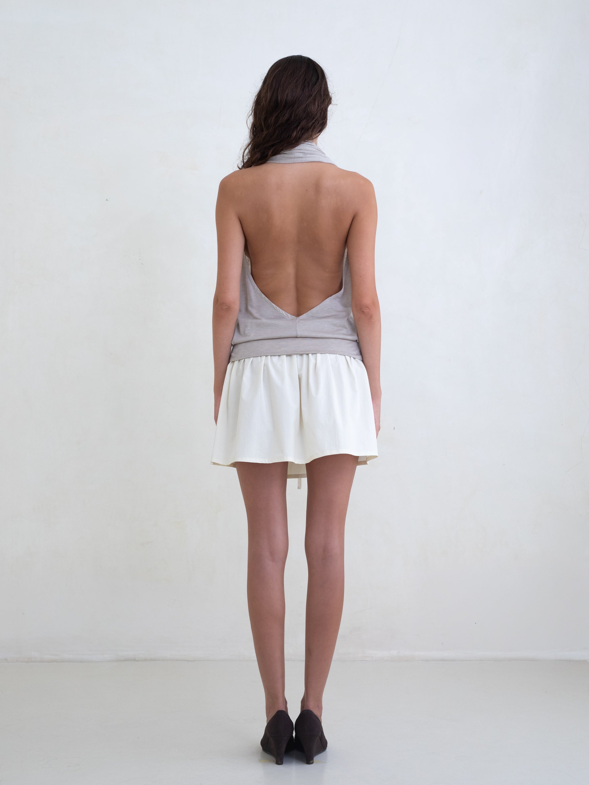 Woman wearing a beige draped halter top and a cream mini skirt on a white background. 