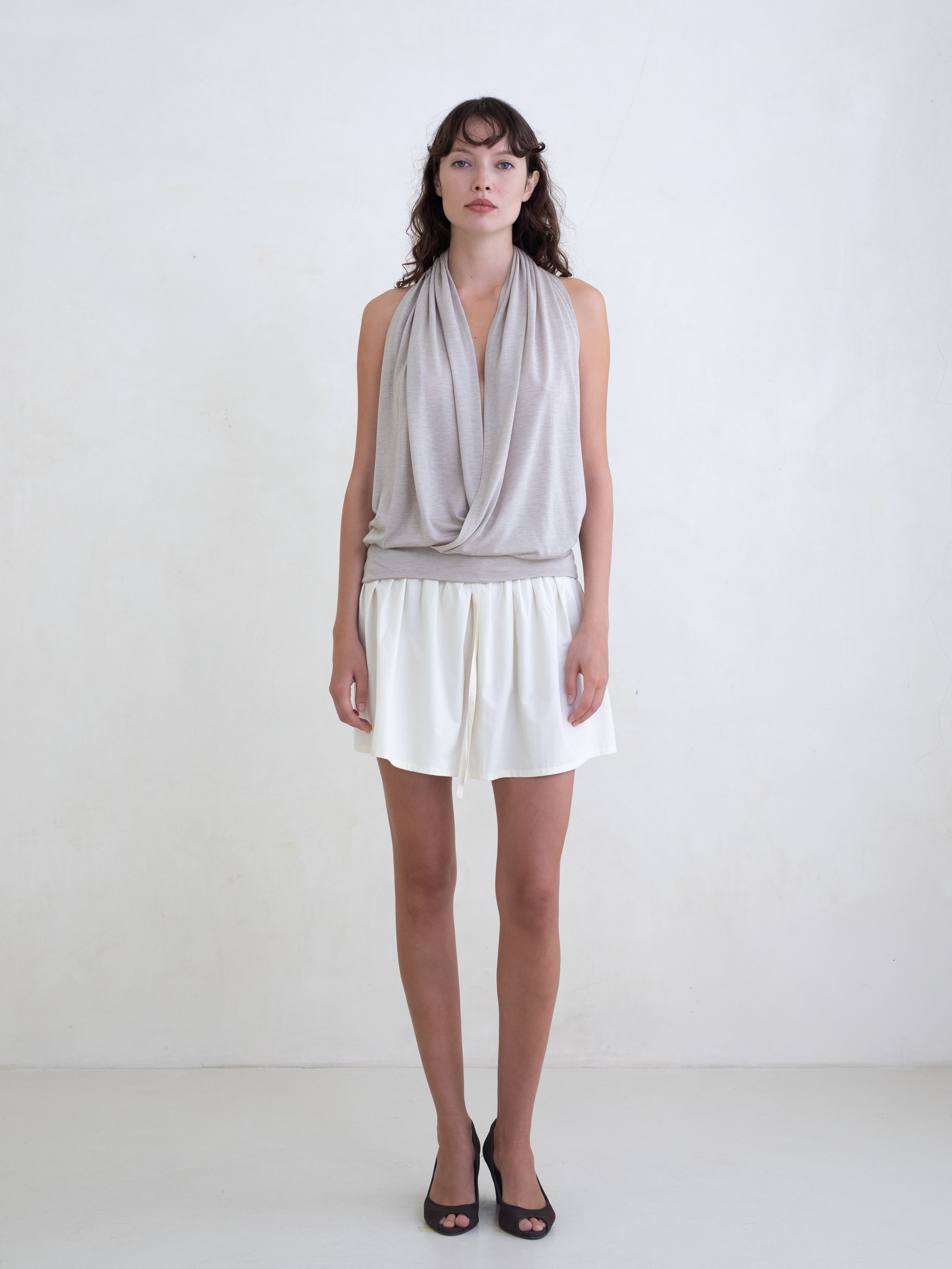 Woman wearing a beige draped halter top and a cream mini skirt on a white background. 