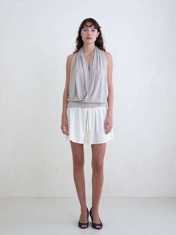 Woman wearing a beige draped halter top and a cream mini skirt on a white background. 