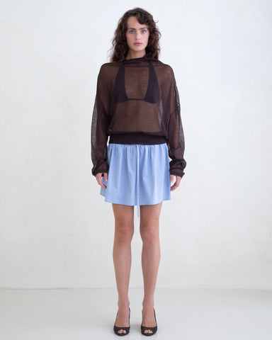 Woman wearing a sheer brown sweater and a light blue mini skirt on a white background. 