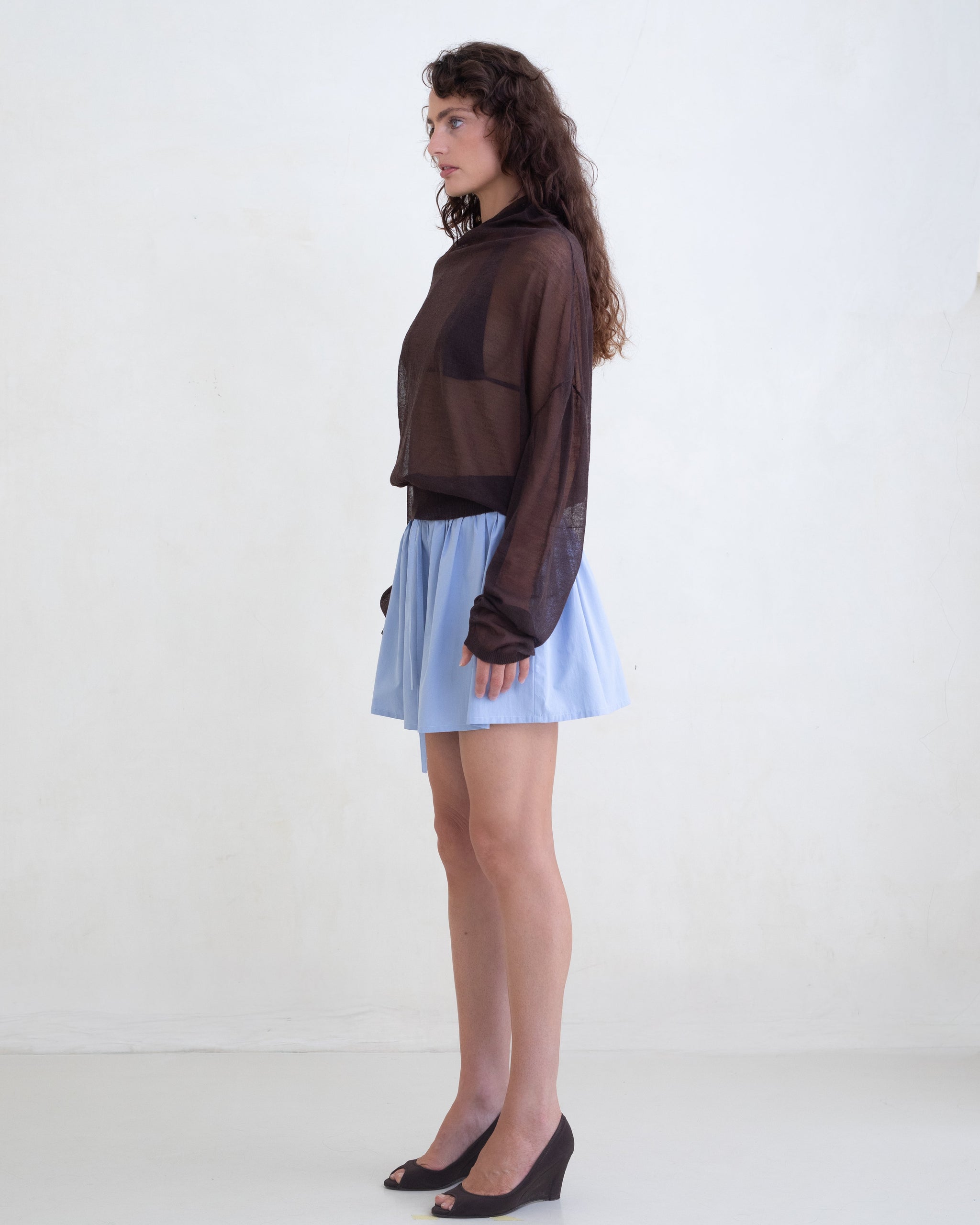 Woman wearing a sheer brown sweater and a light blue mini skirt on a white background. 
