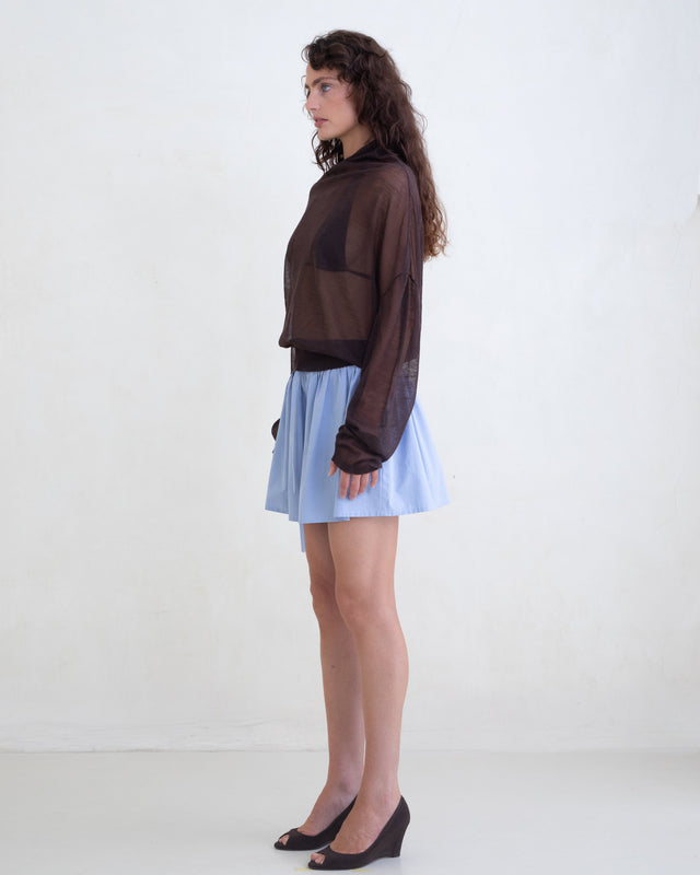 Woman wearing a sheer brown sweater and a light blue mini skirt on a white background. 