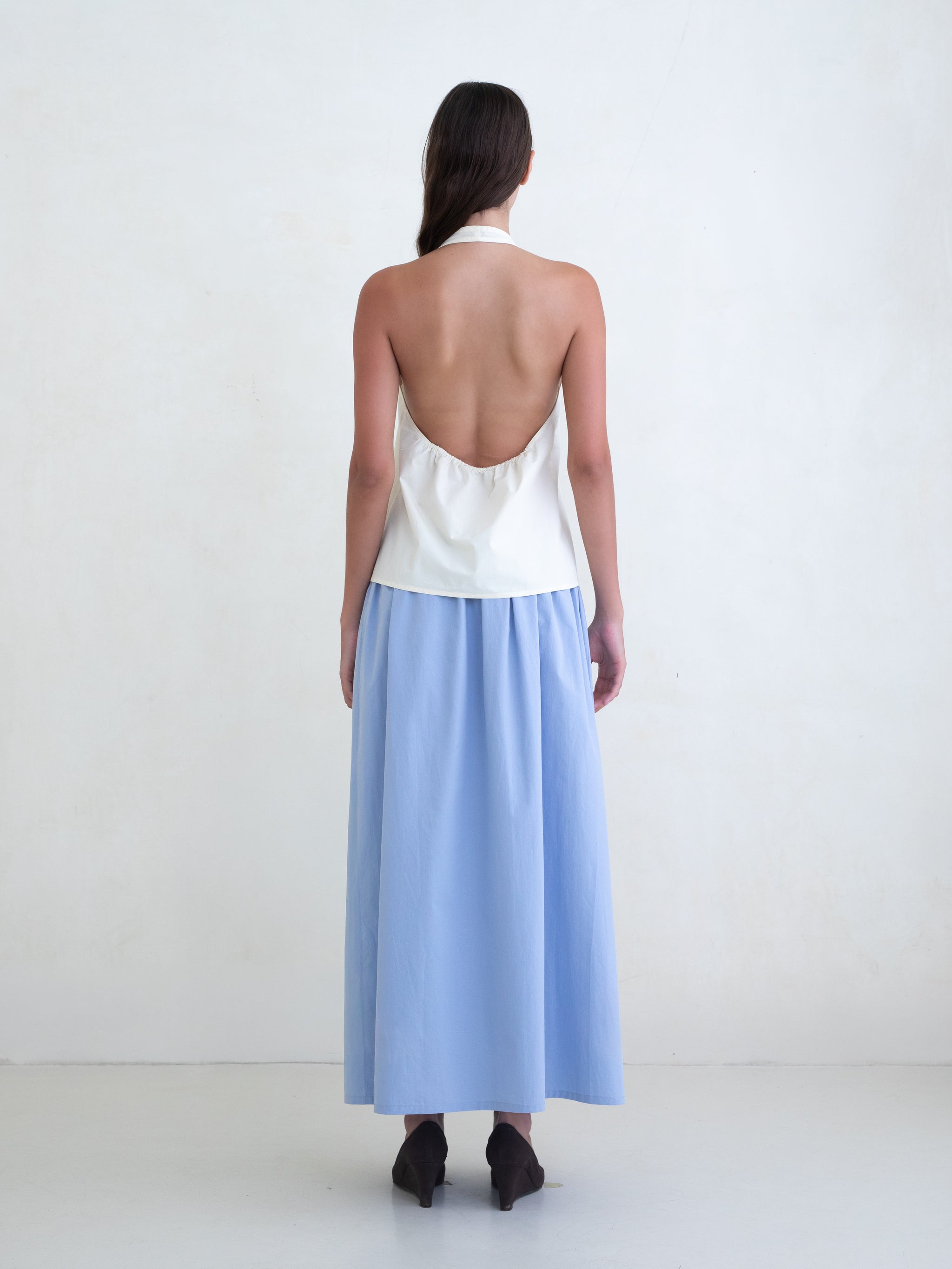 Woman wearing a cream v-neck halter top and a light blue maxi skirt on a white background. 