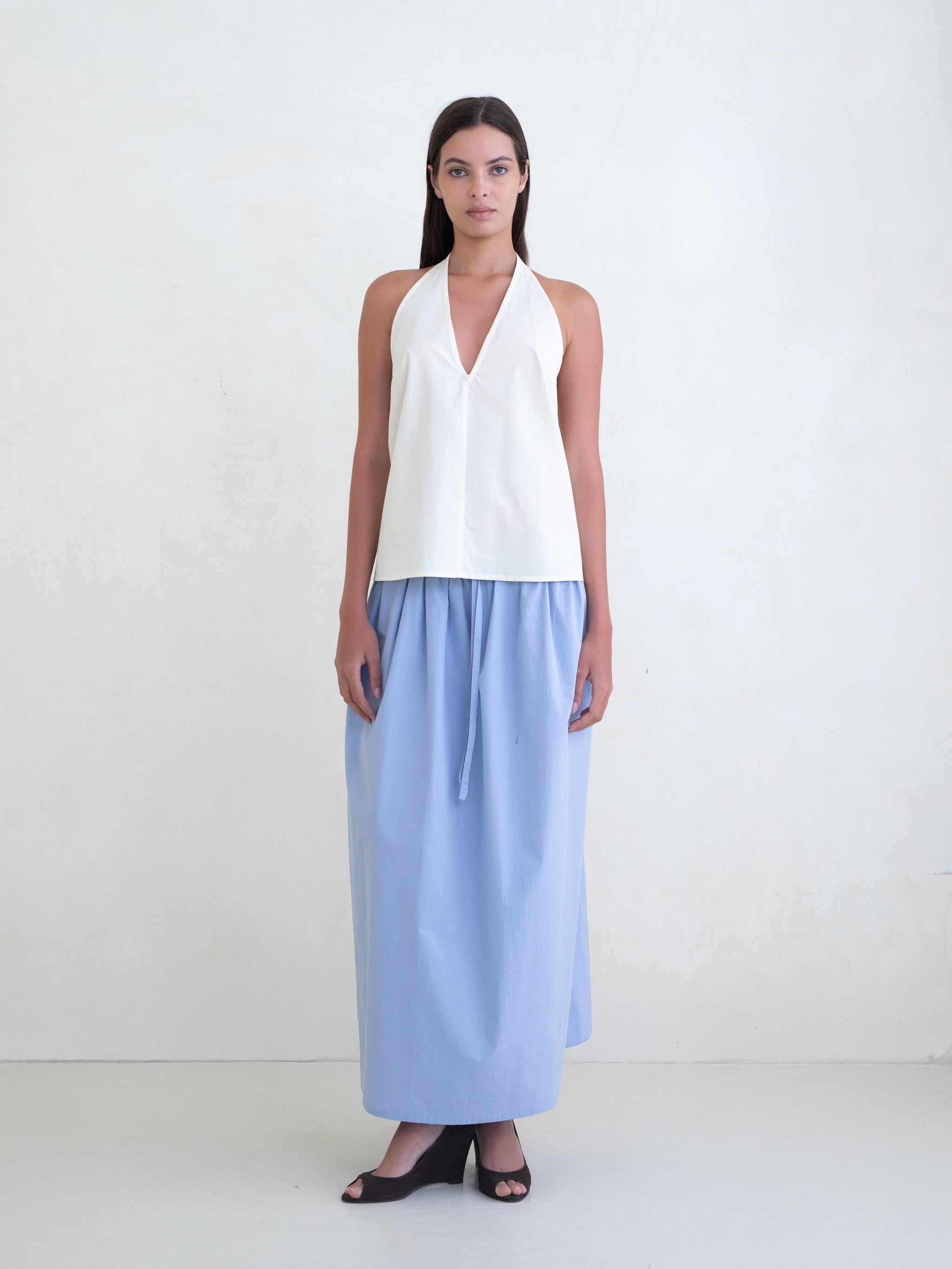 Woman wearing a cream v-neck halter top and a light blue maxi skirt on a white background. 