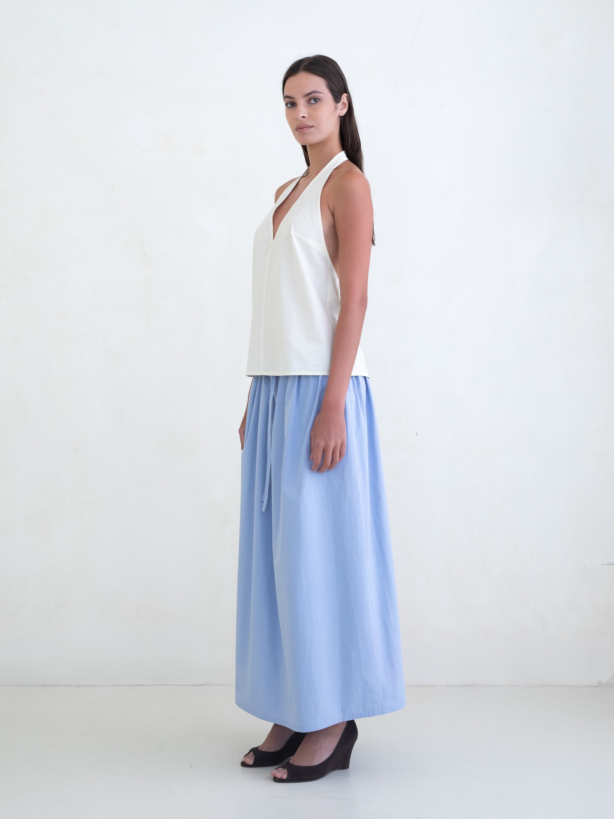Woman wearing a cream v-neck halter top and a light blue maxi skirt on a white background. 