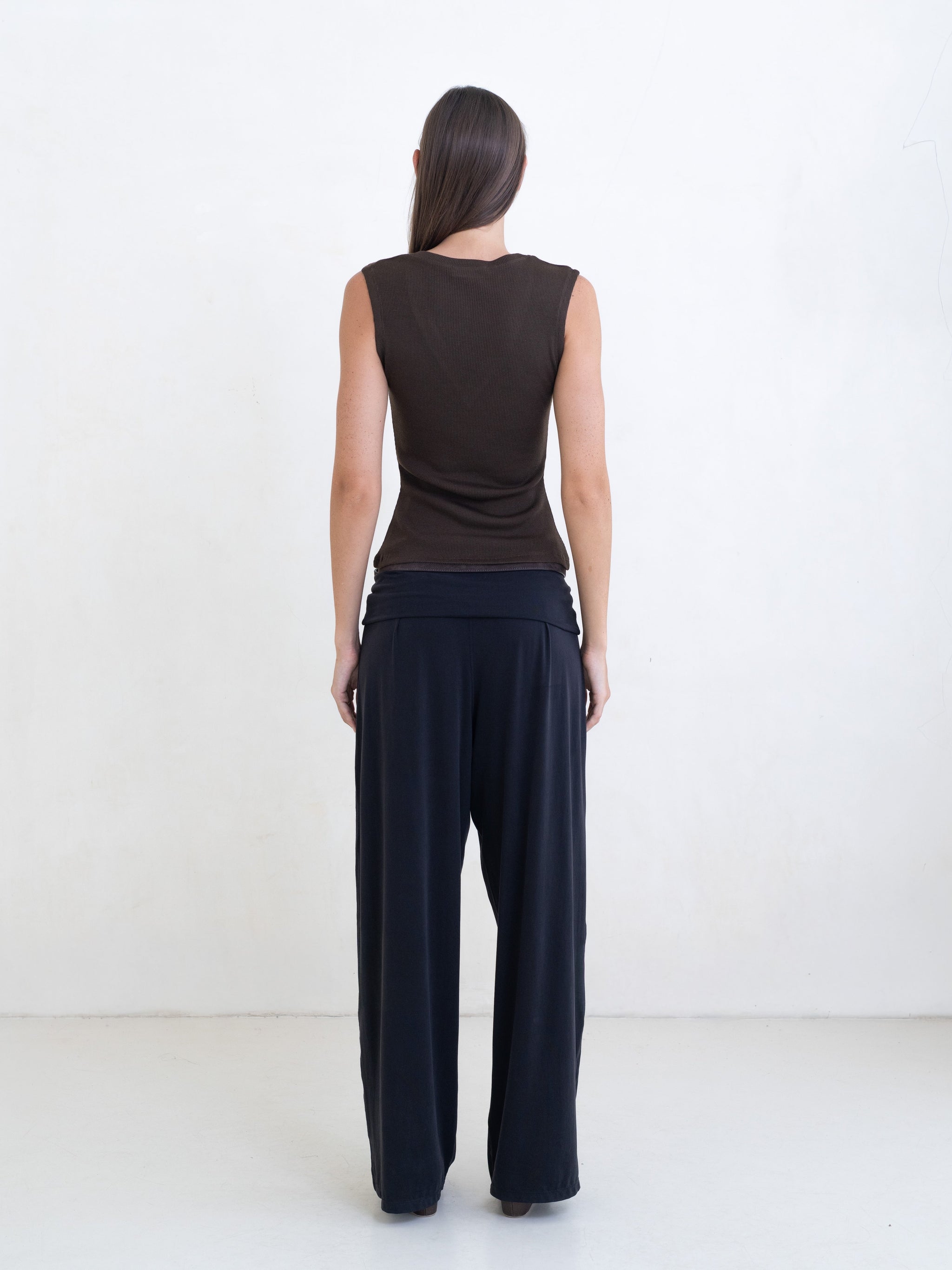 Woman wearing a brown sleeveless v-neck top, black pants with a brown leather belt on a white background. 