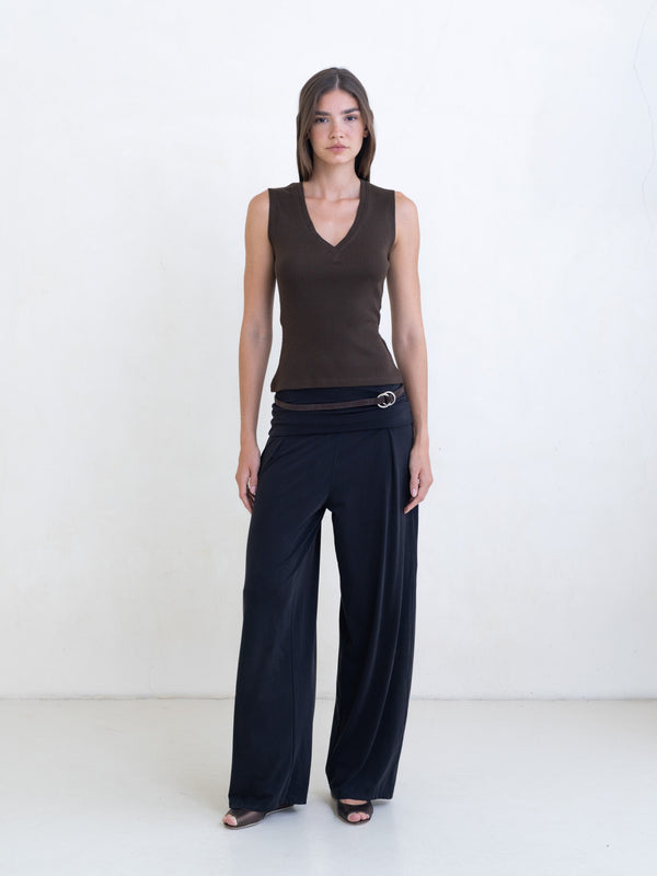 Woman wearing a brown sleeveless v-neck top, black pants with a brown leather belt on a white background. 