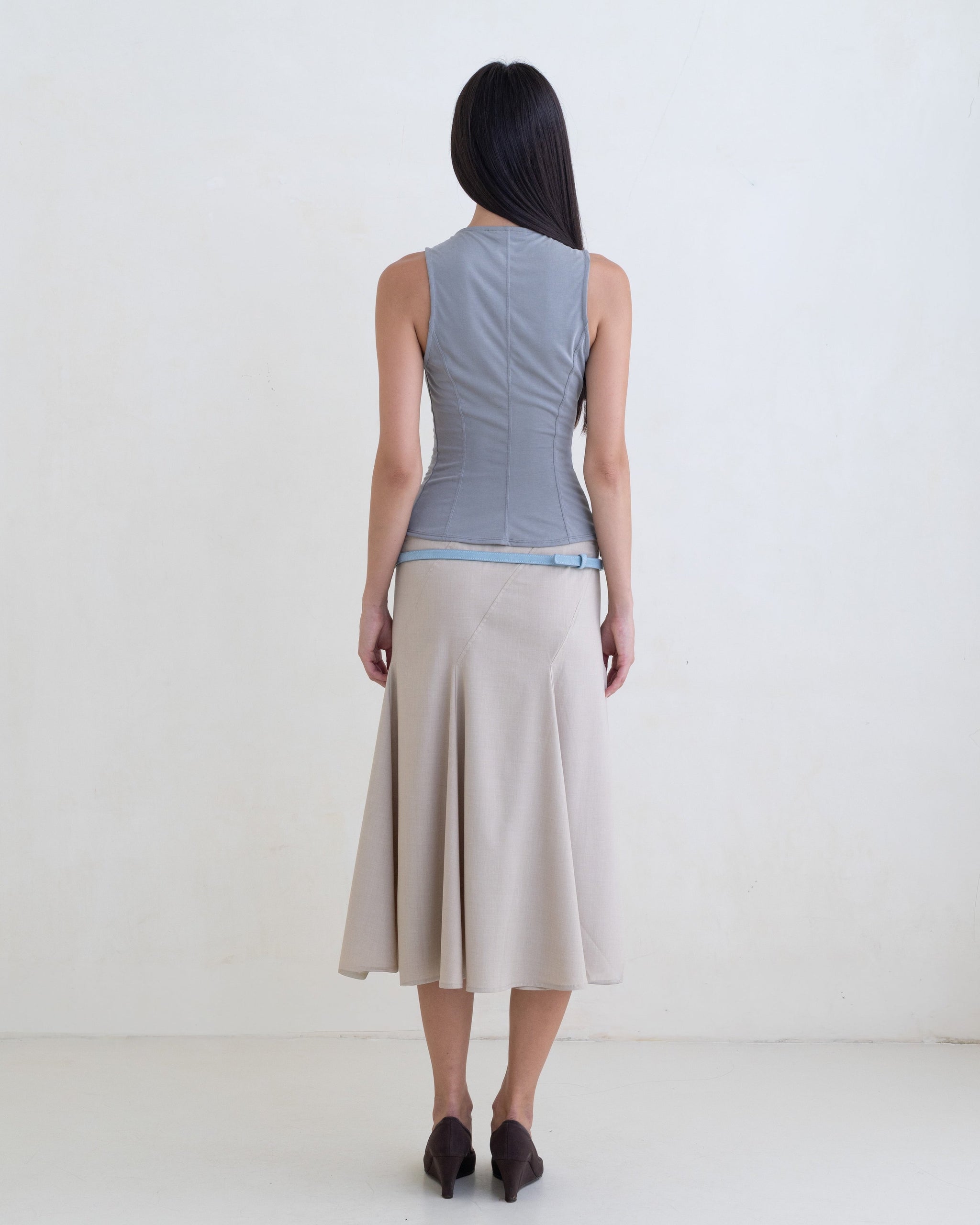 Woman wearing a gray sleeveless top, beige skirt with a light blue leather belt on a white background. 