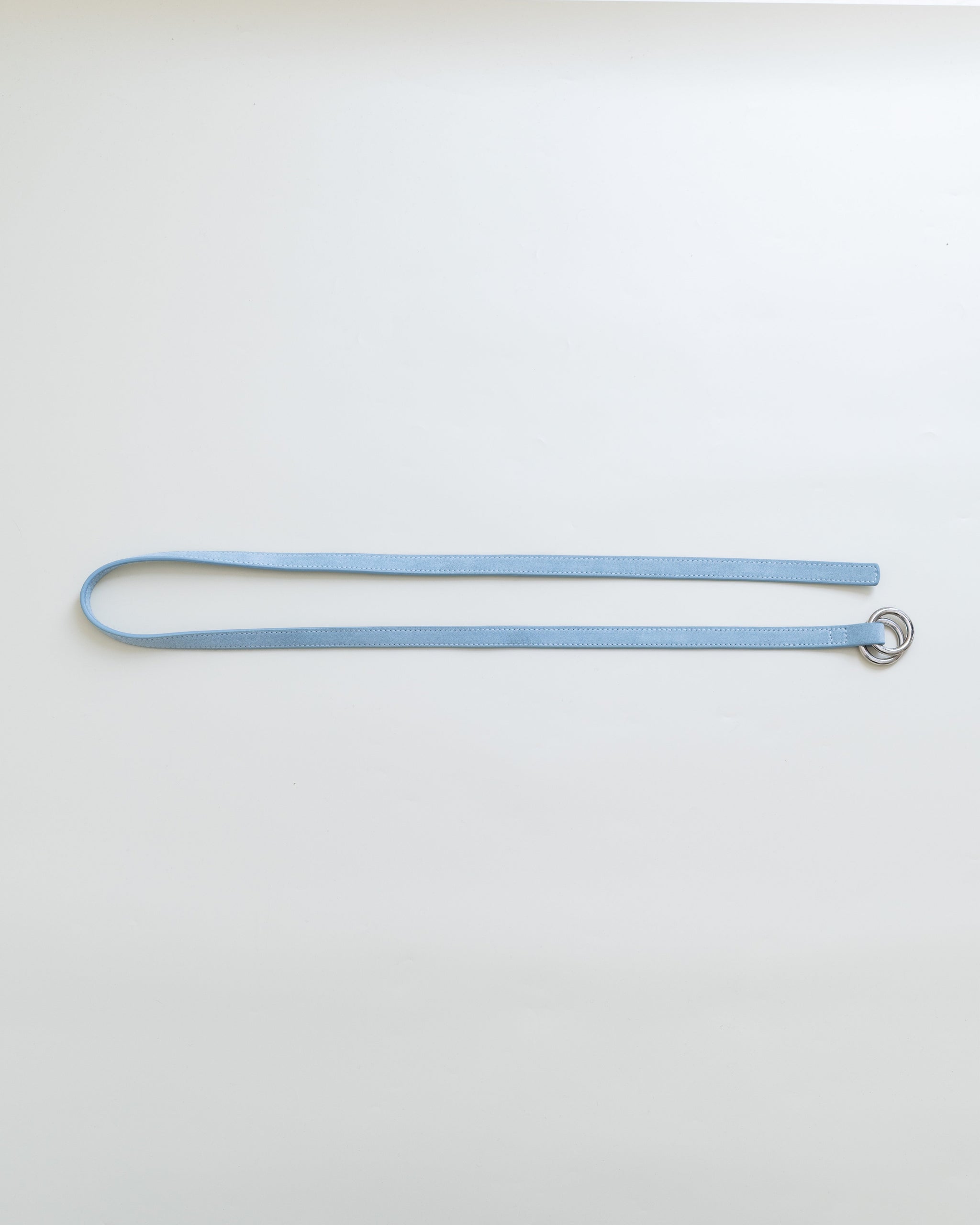 A light blue leather belt with dual metal loop closure on a white background. 