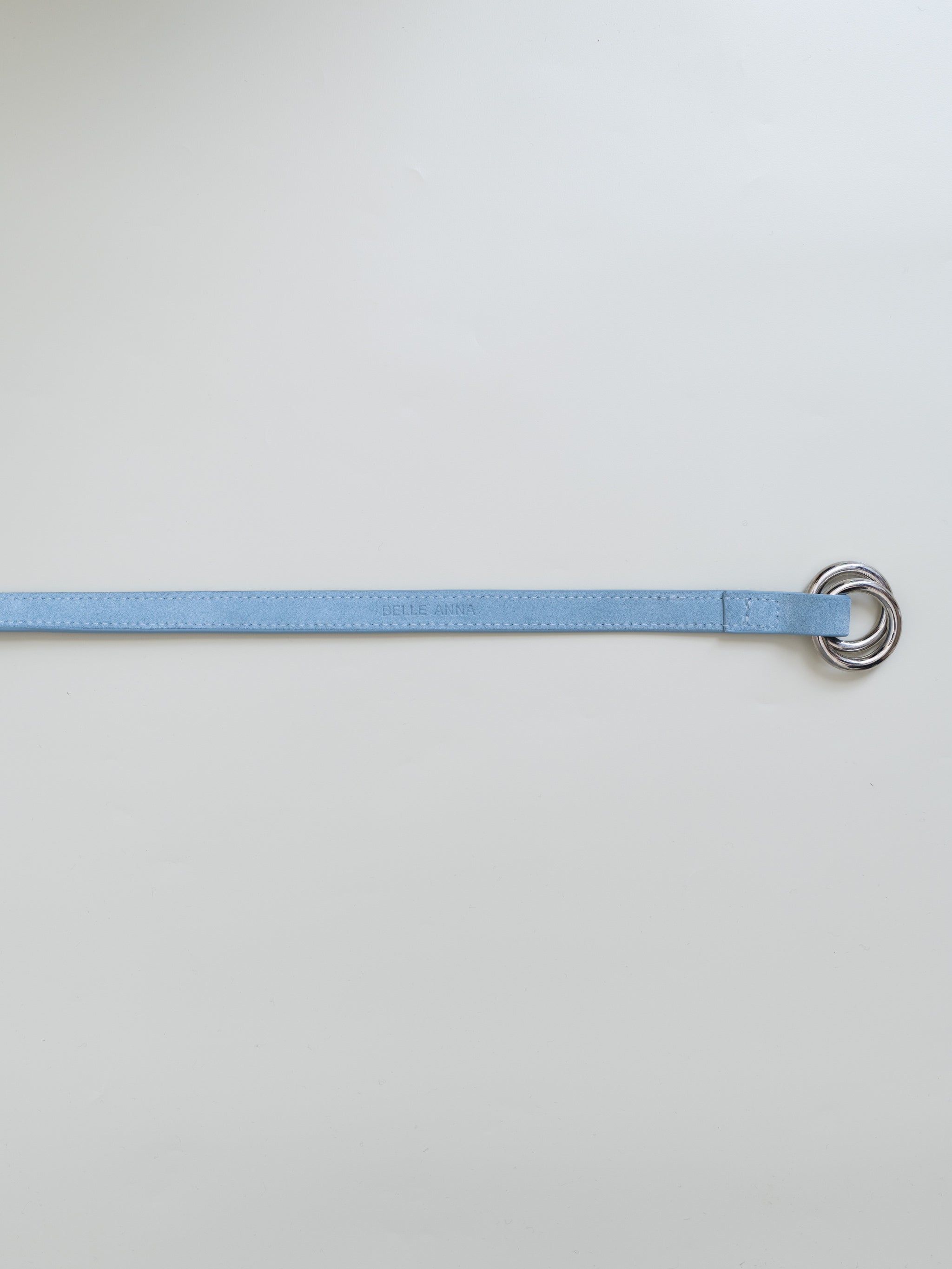A light blue leather belt with dual metal loop closure on a white background. 