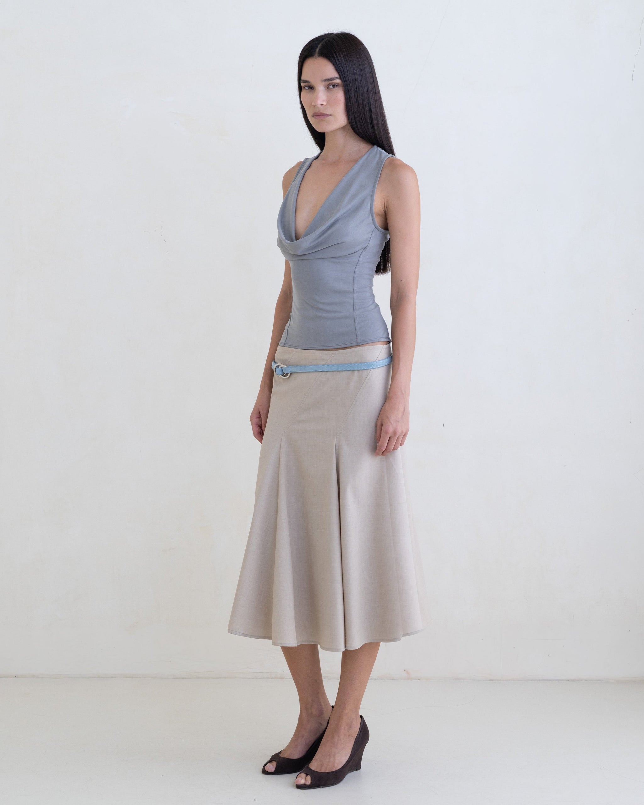 Woman wearing a gray sleeveless top, beige skirt with a light blue leather belt on a white background. 