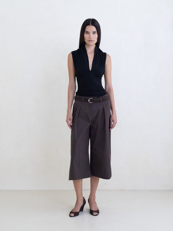 Woman wearing a black sleeveless top and brown wide-leg cropped trousers on a white background. 