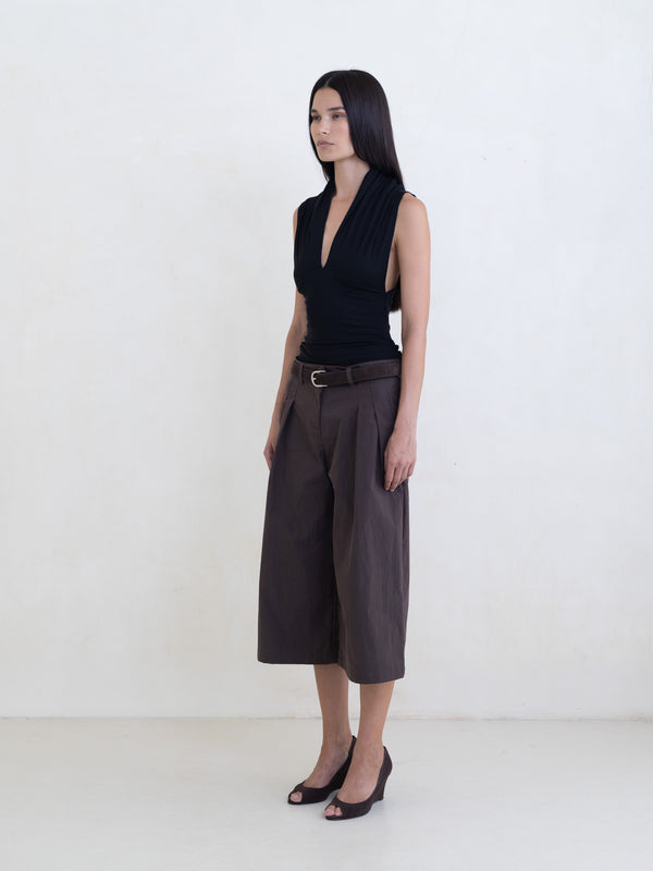 Woman wearing a black sleeveless top and brown wide-leg cropped trousers on a white background. 