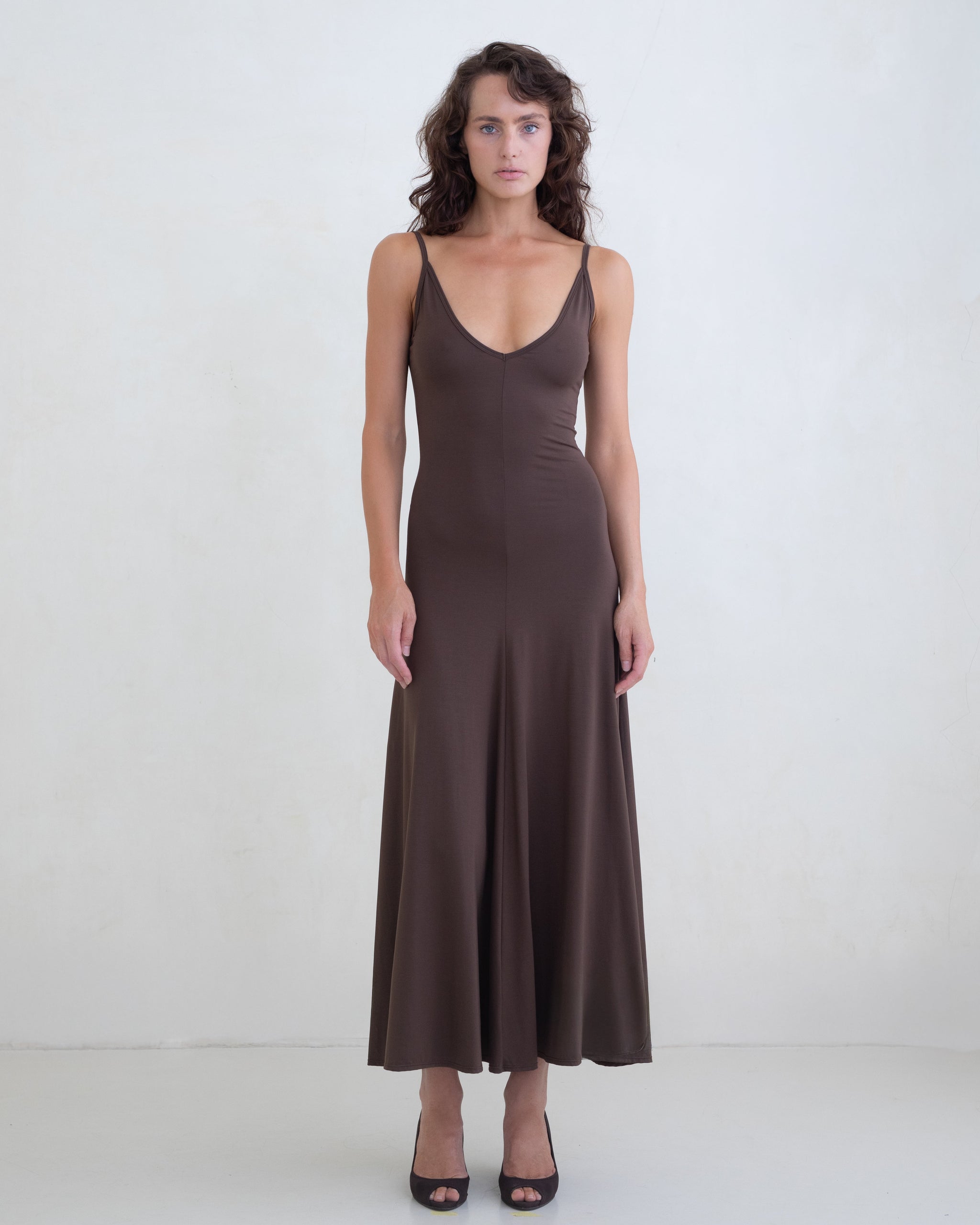 Woman wearing a brown scoop neck slip dress on a white background. 