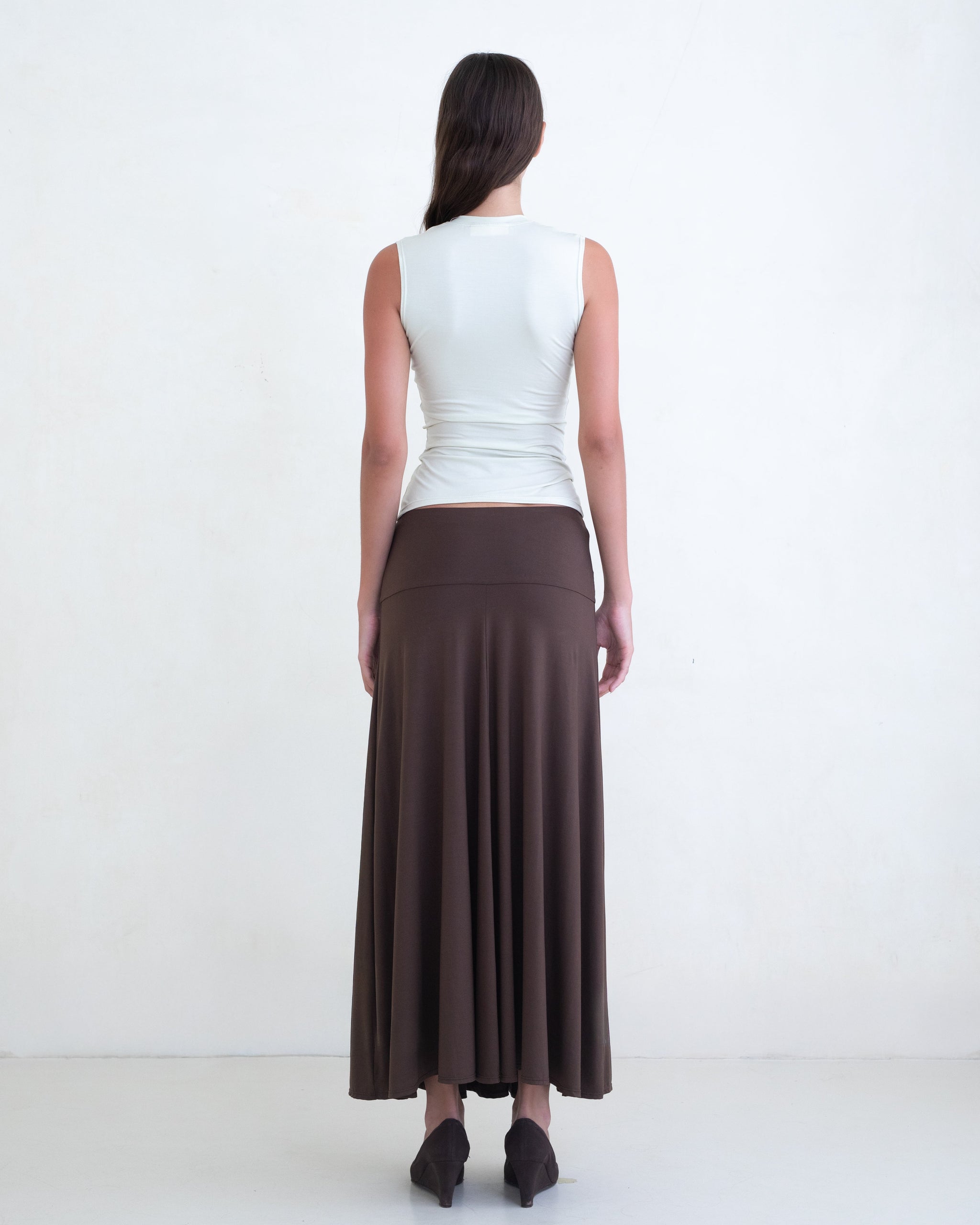 Woman wearing a light green V-neck top and a brown maxi skirt on a white background. 