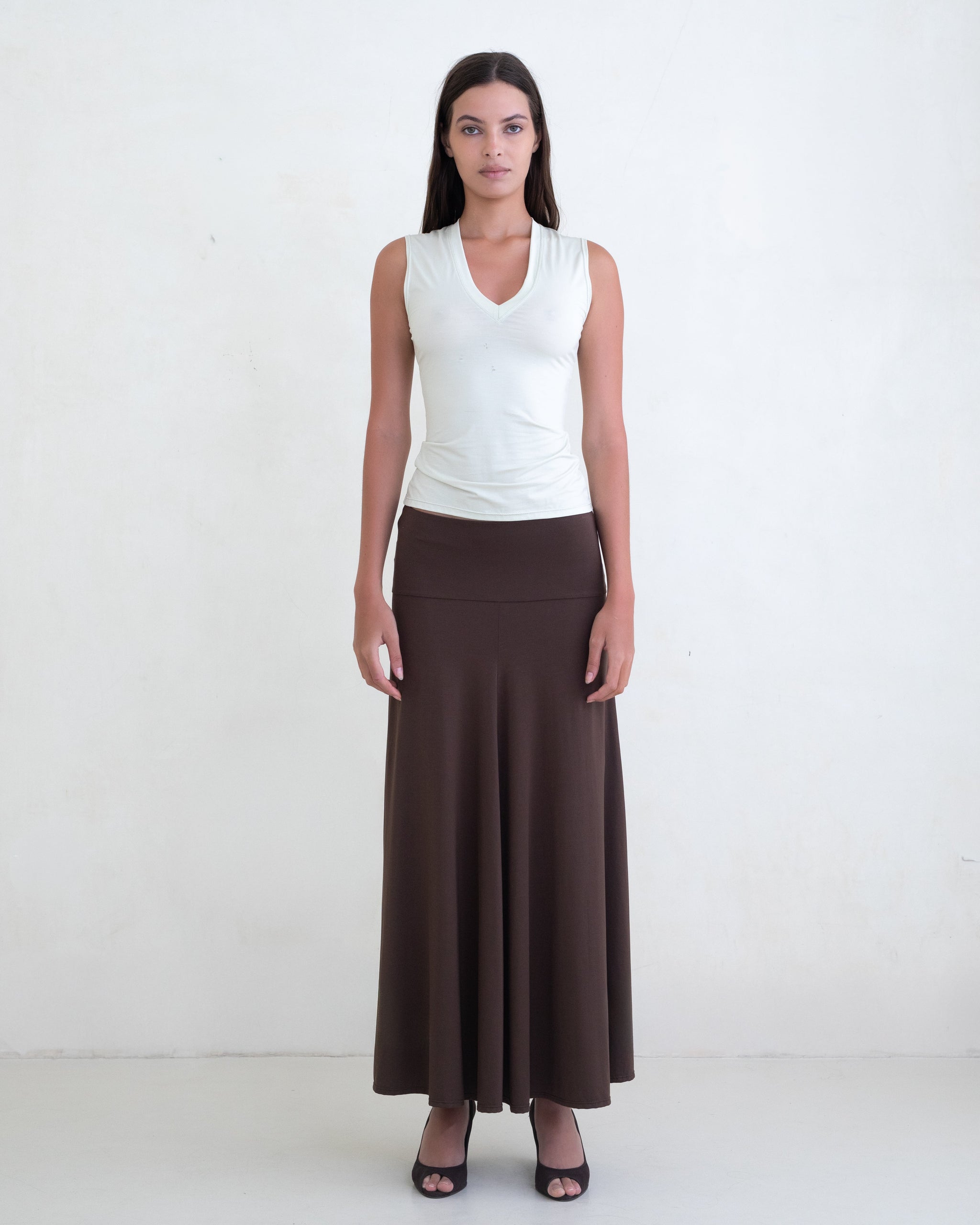 Woman wearing a light green V-neck top and a brown maxi skirt on a white background. 
