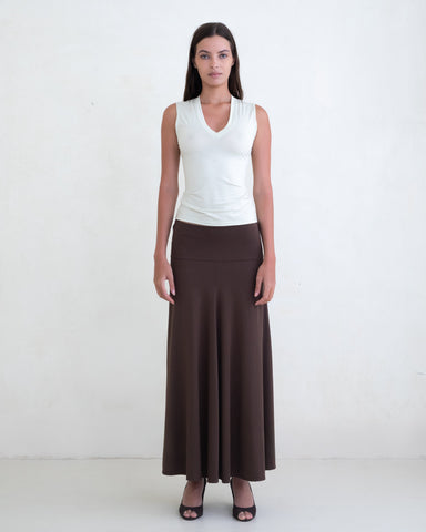 Woman wearing a light green V-neck top and a brown maxi skirt on a white background. 