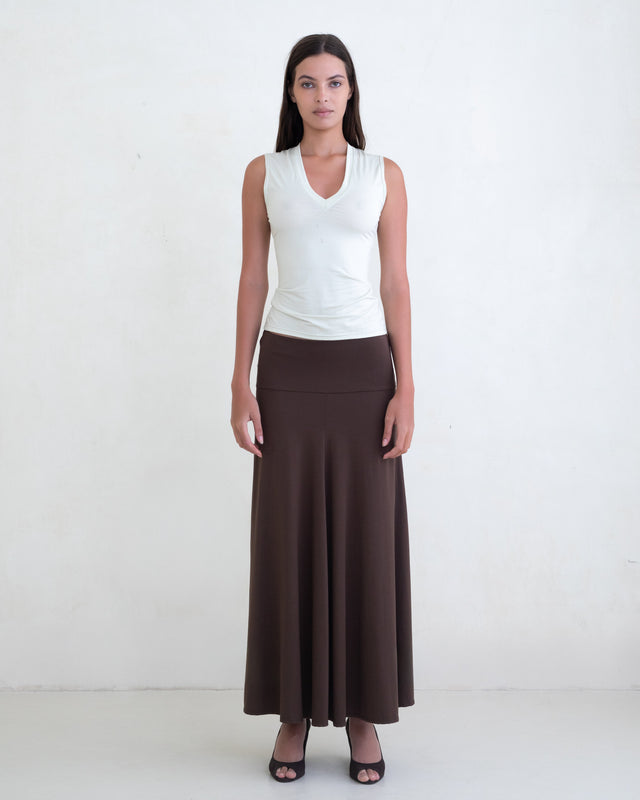 Woman wearing a light green V-neck top and a brown maxi skirt on a white background. 