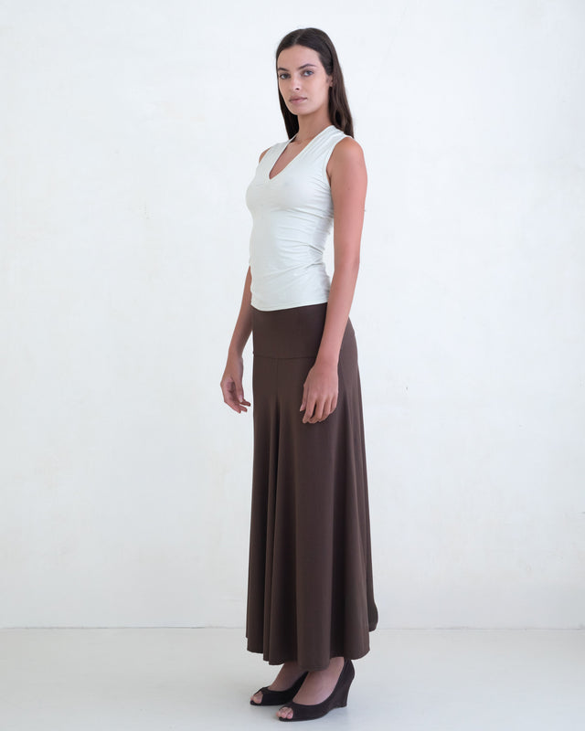 Woman wearing a light green V-neck top and a brown maxi skirt on a white background. 