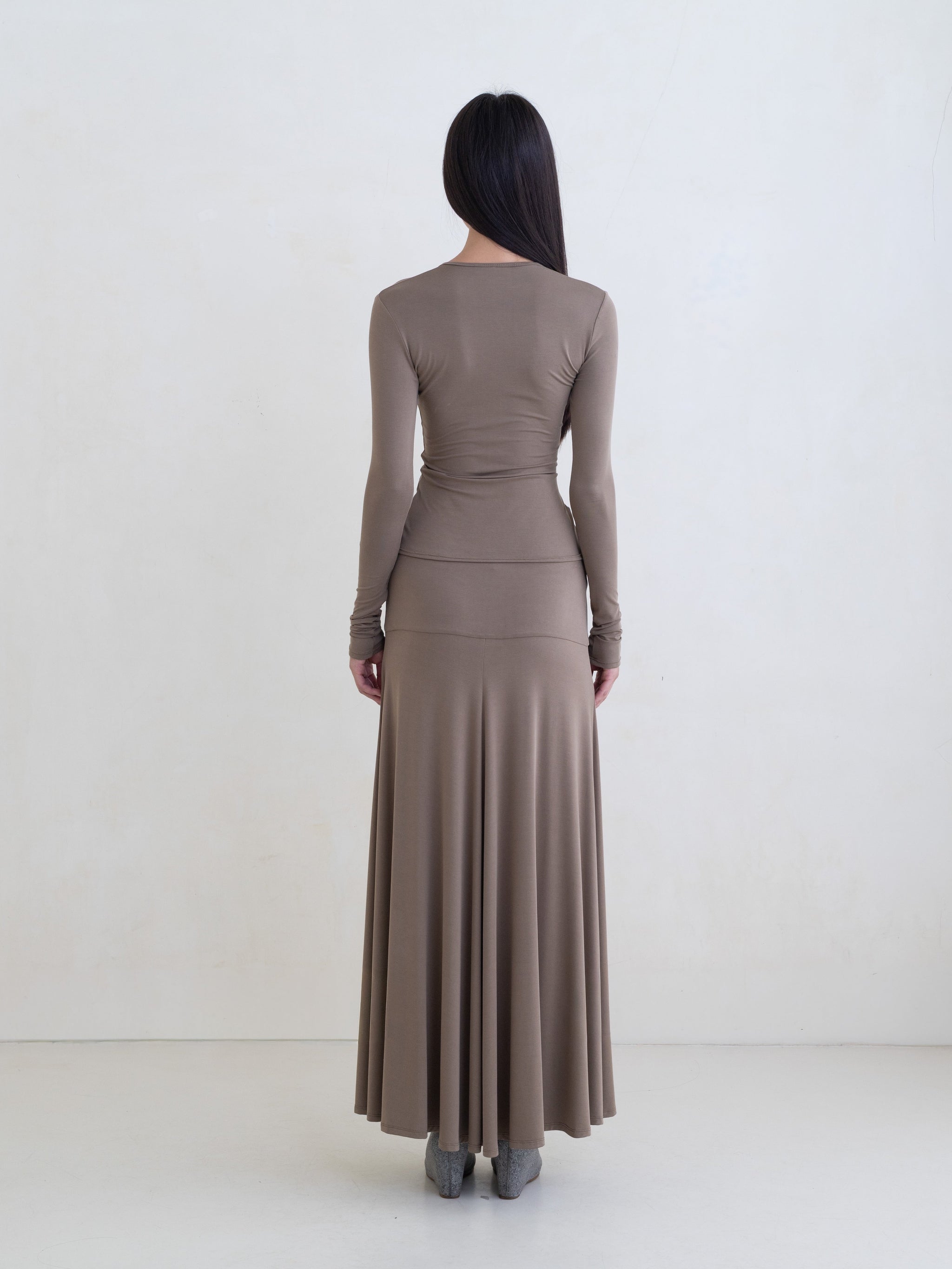 Woman wearing a taupe long sleeve top and a taupe maxi skirt on a white background.
