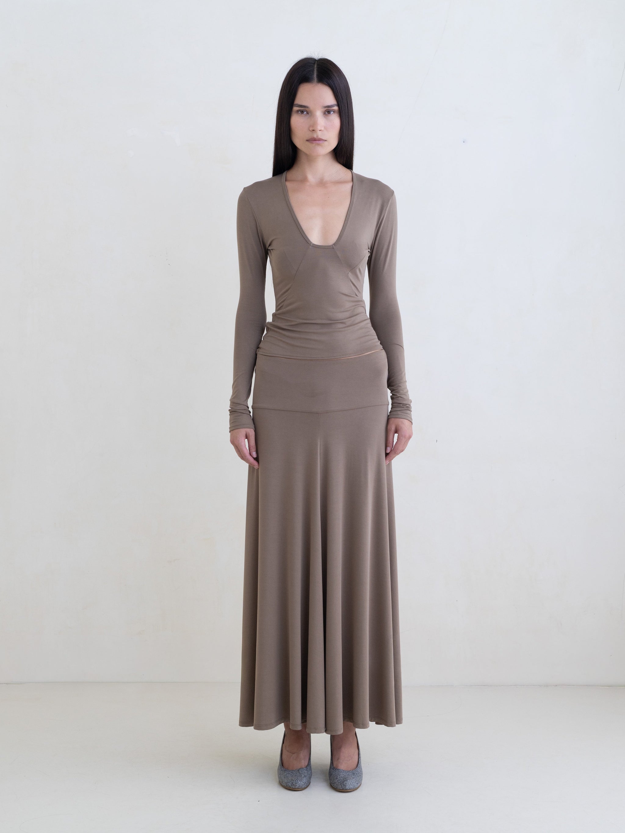Woman wearing a taupe long sleeve top and a taupe maxi skirt on a white background.