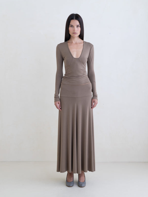 Woman wearing a taupe long sleeve top and a taupe maxi skirt on a white background.